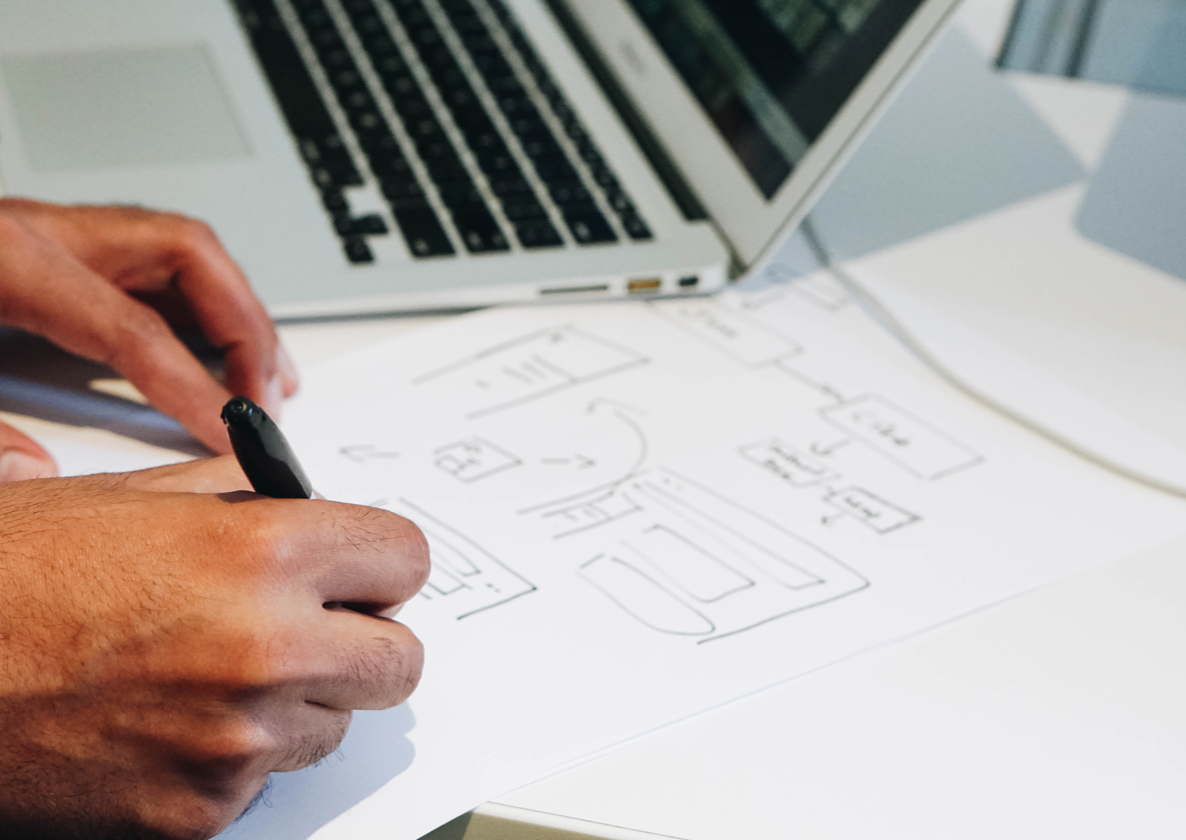 A person writing on a piece of paper next to a laptop.