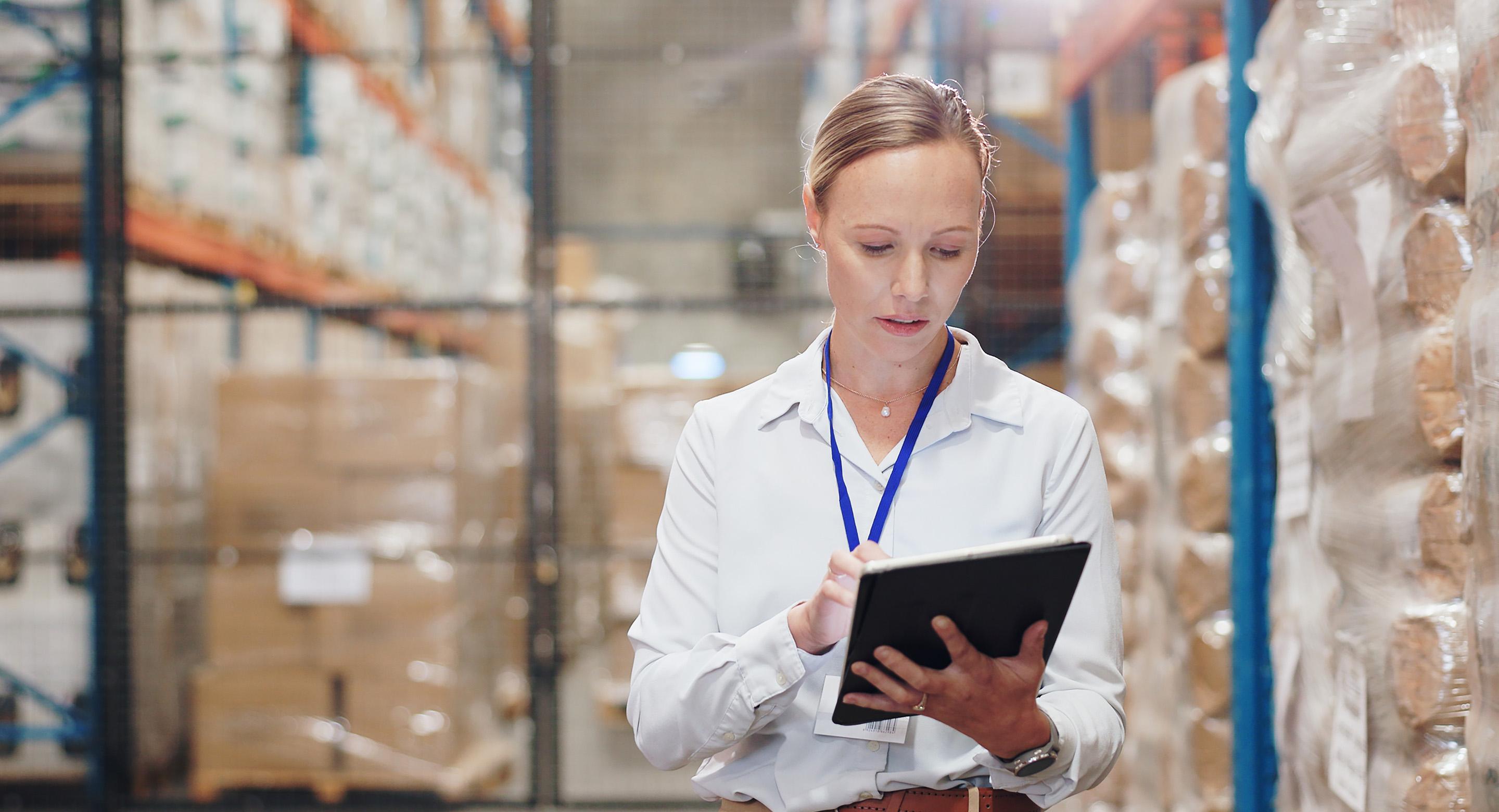 Warehouse worker using a tablet to check inventory in a storage aisle.