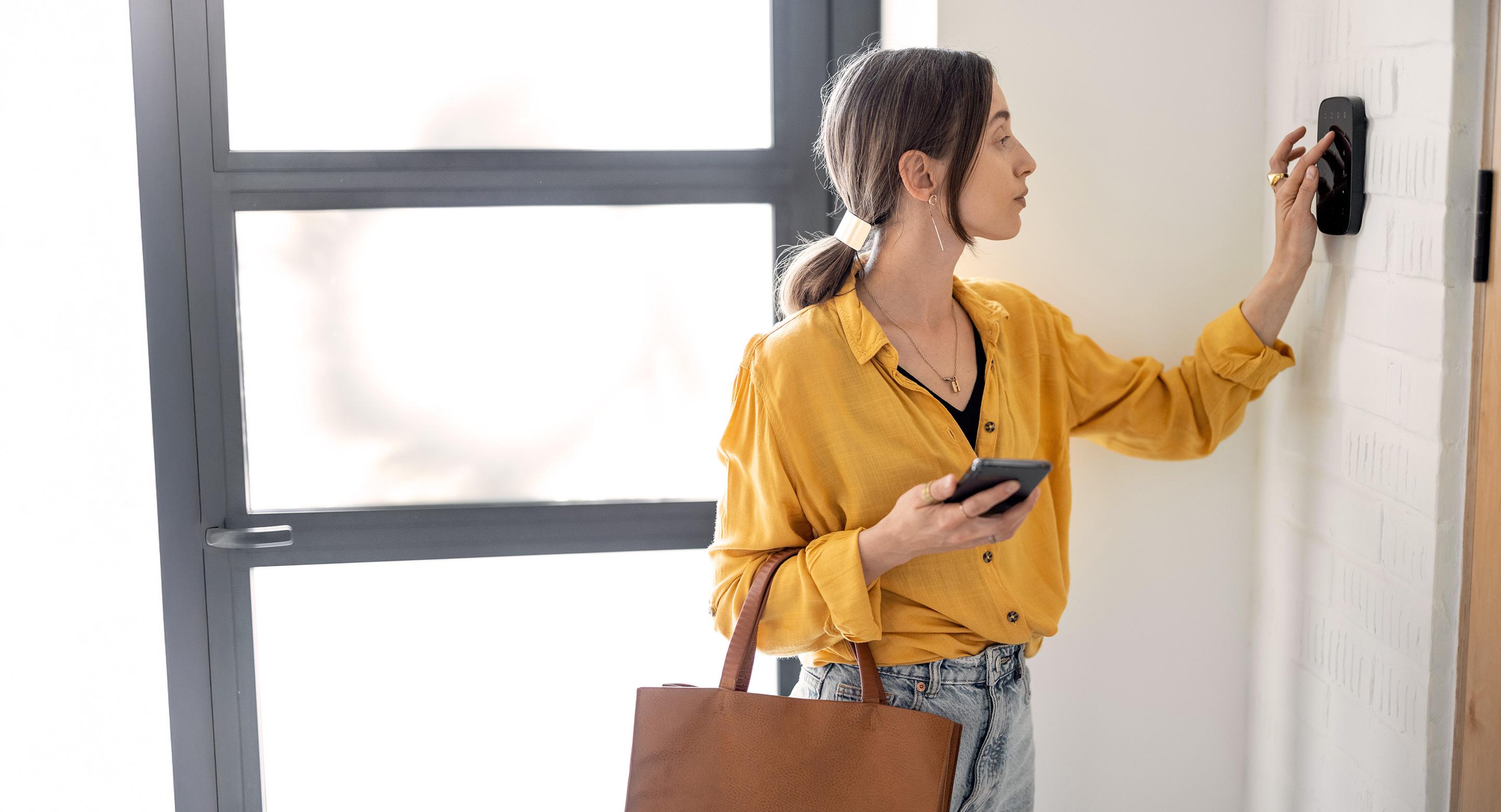 A woman uses a key pad on her home security device.