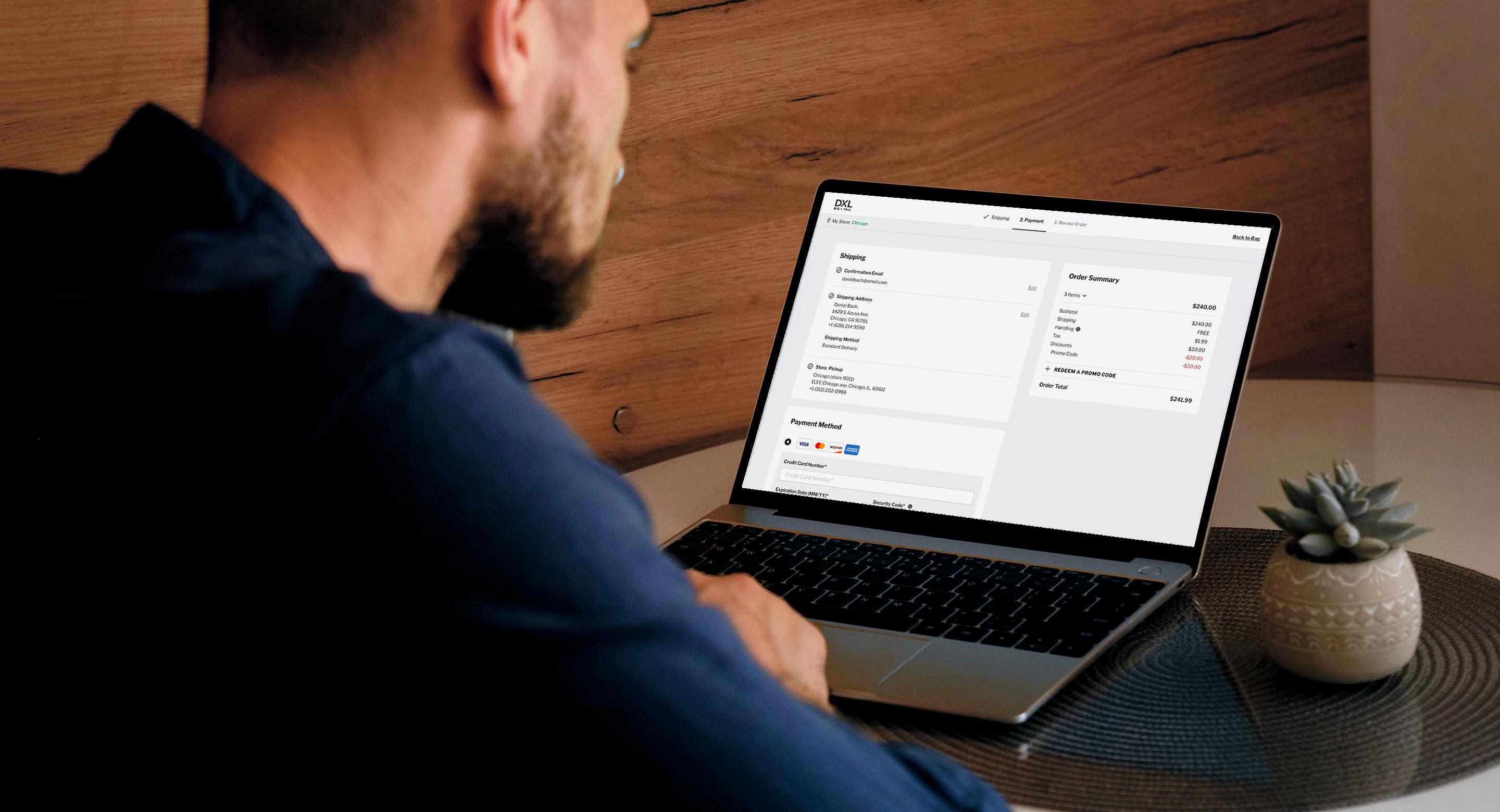A man is seated at a table using a laptop to view an online checkout page with an order summary.