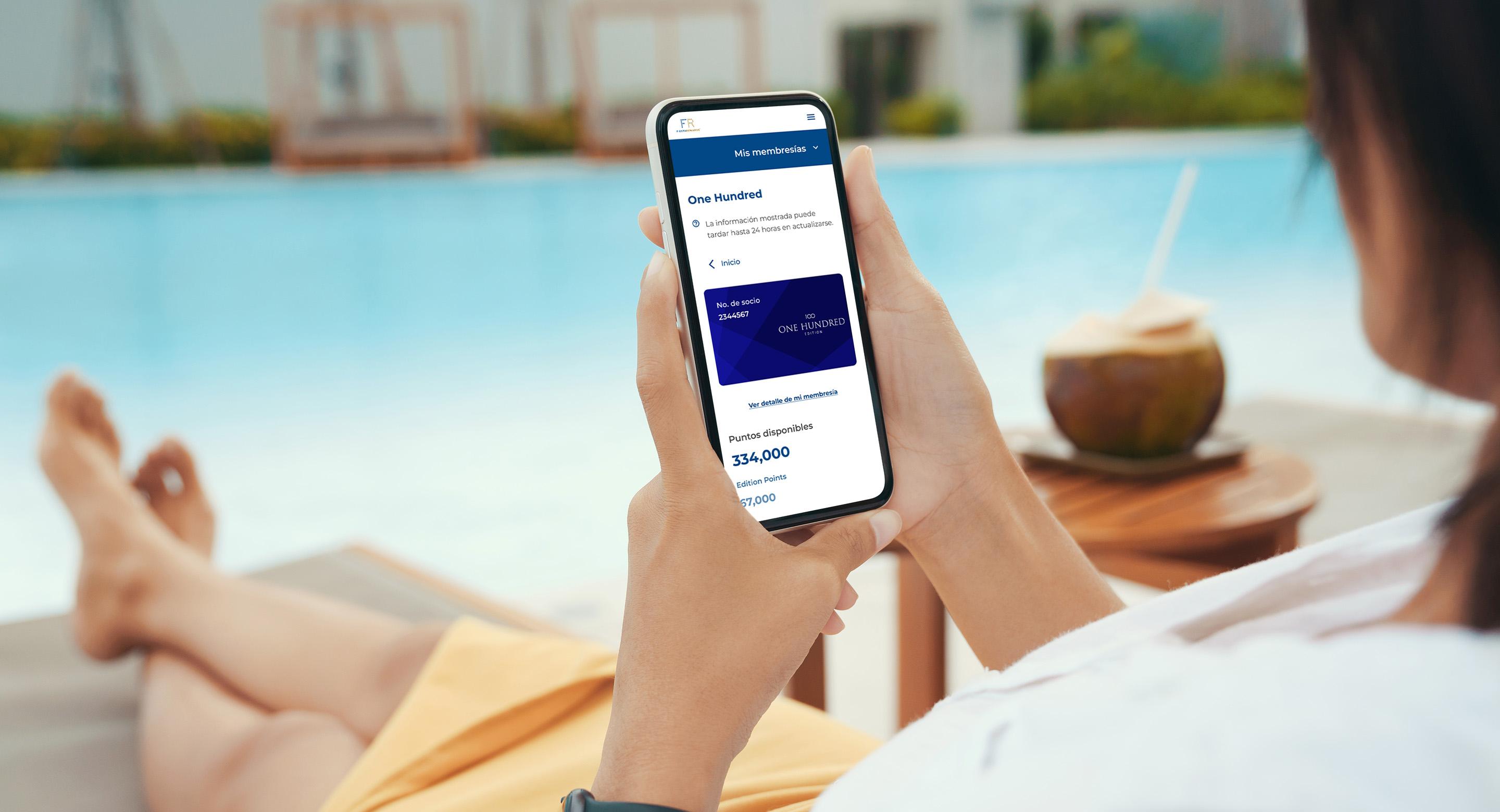 Una mujer sentada junto a la piscina con su teléfono inteligente en la mano revisando su cuenta de fidelidad de Grupo Posadas