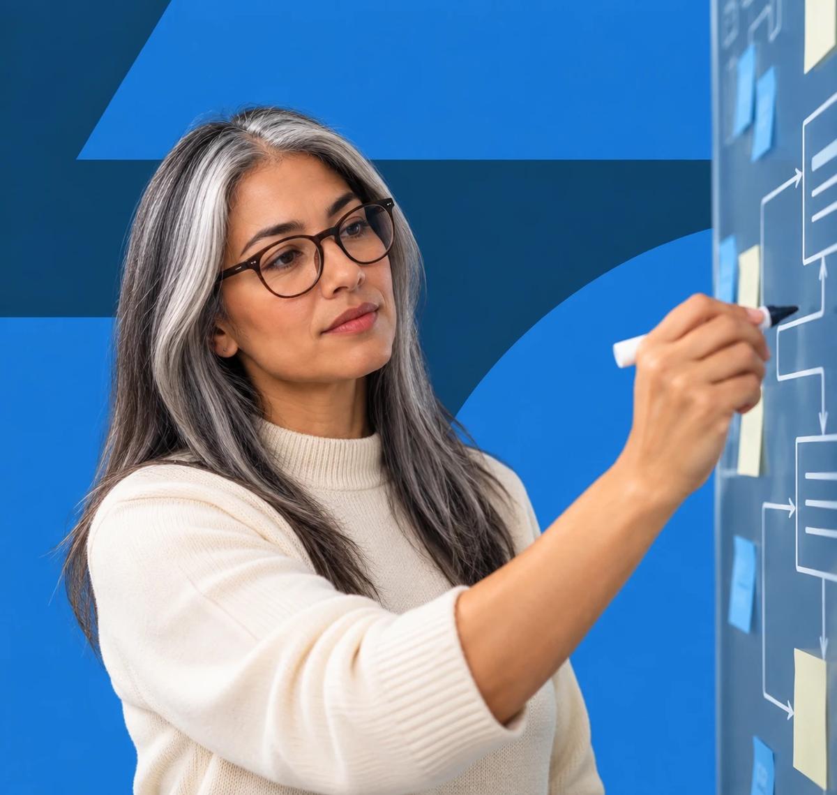Una mujer dibujando un diagrama de flujo de datos en un tablero de vidrio cubierto de notas adhesivas.