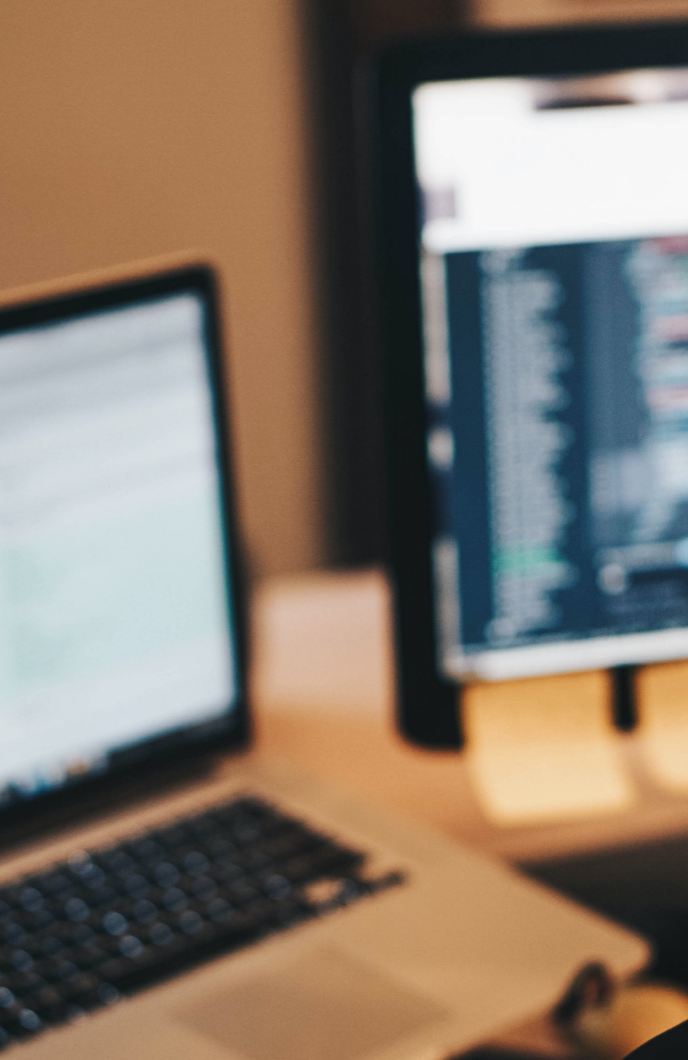 A blurred laptop and monitor on a desk.