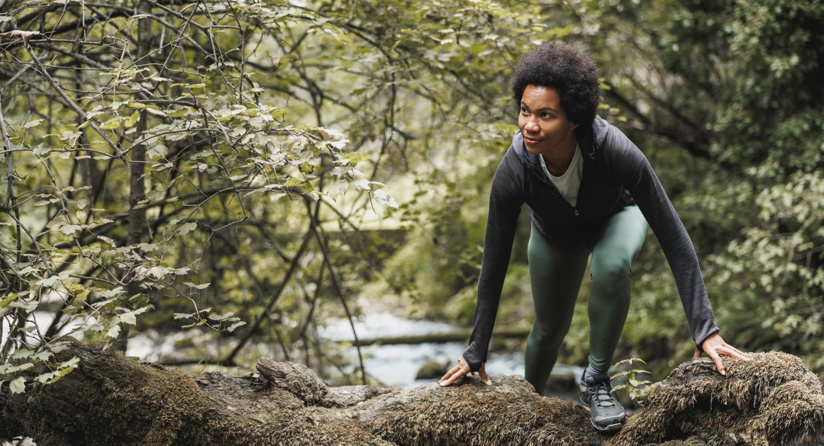 A person in hiking attire stepping onto a rock in a forrested trail.