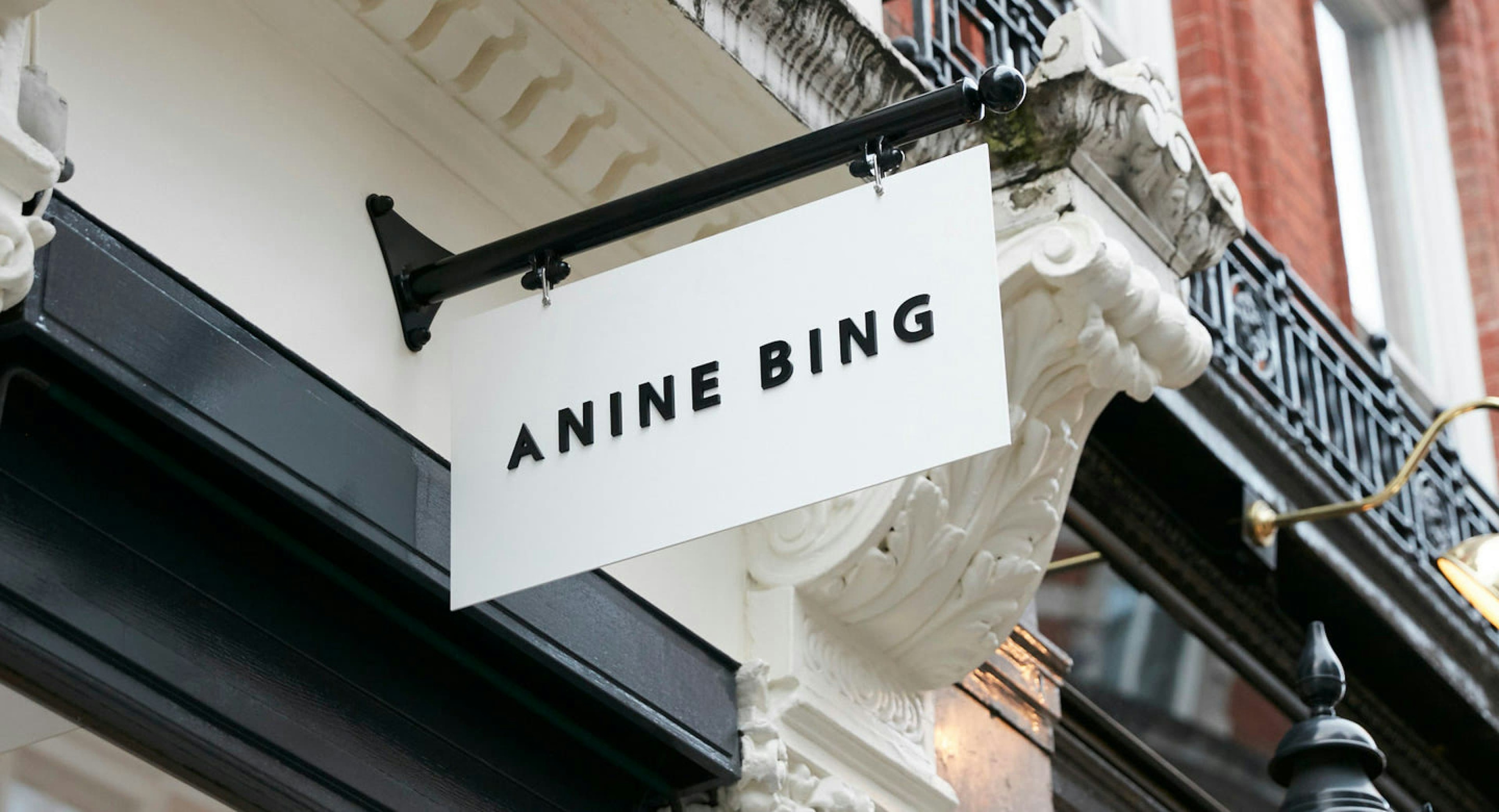 An ANINE BING store sign hanging outside the storefront on a street.