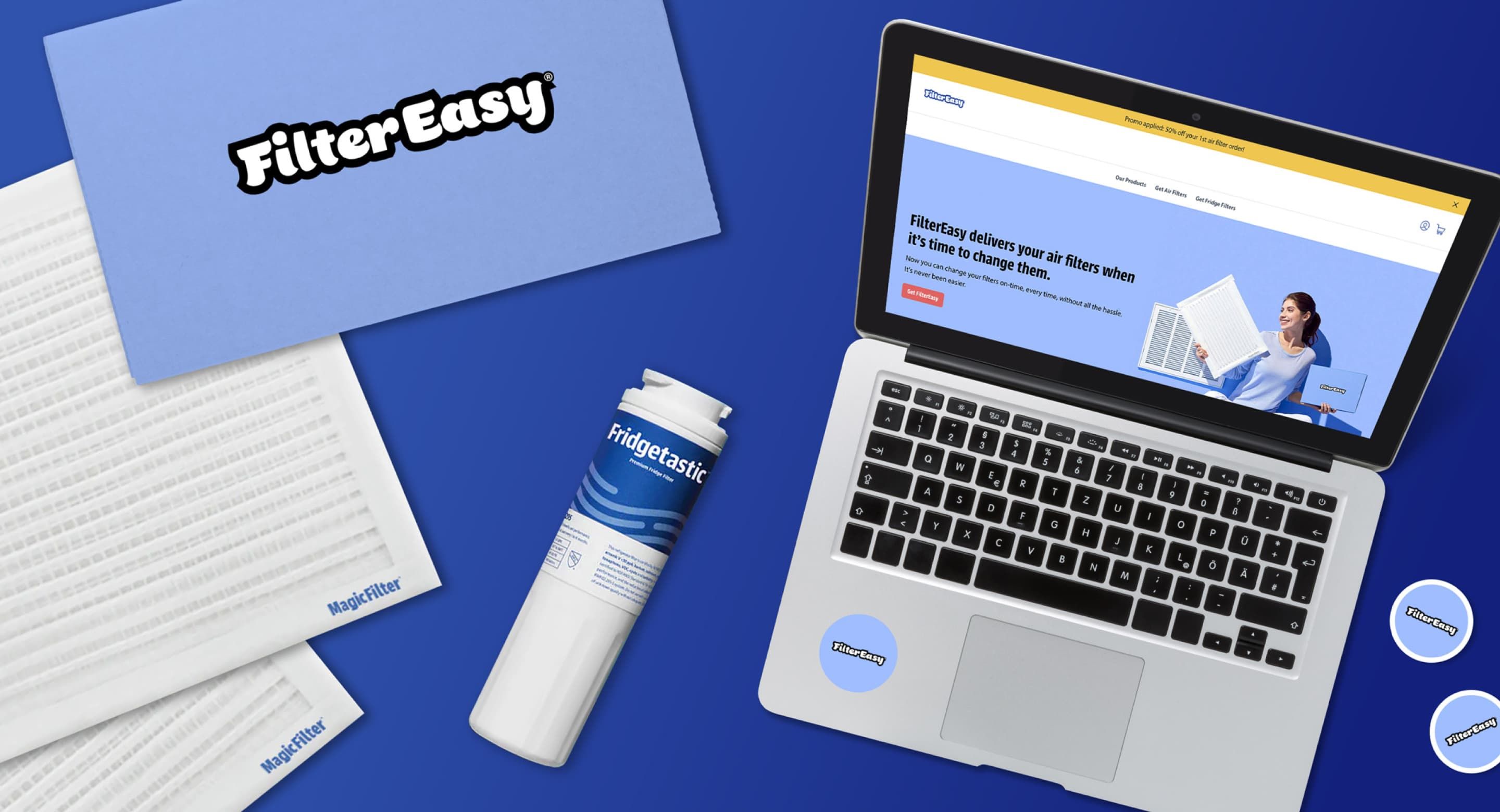 Flatylay featuring a FilterEasy subscription box, a Fridgetastic filter, two Magic Filters, and a laptop screen with the FilterEasy homepage on display.