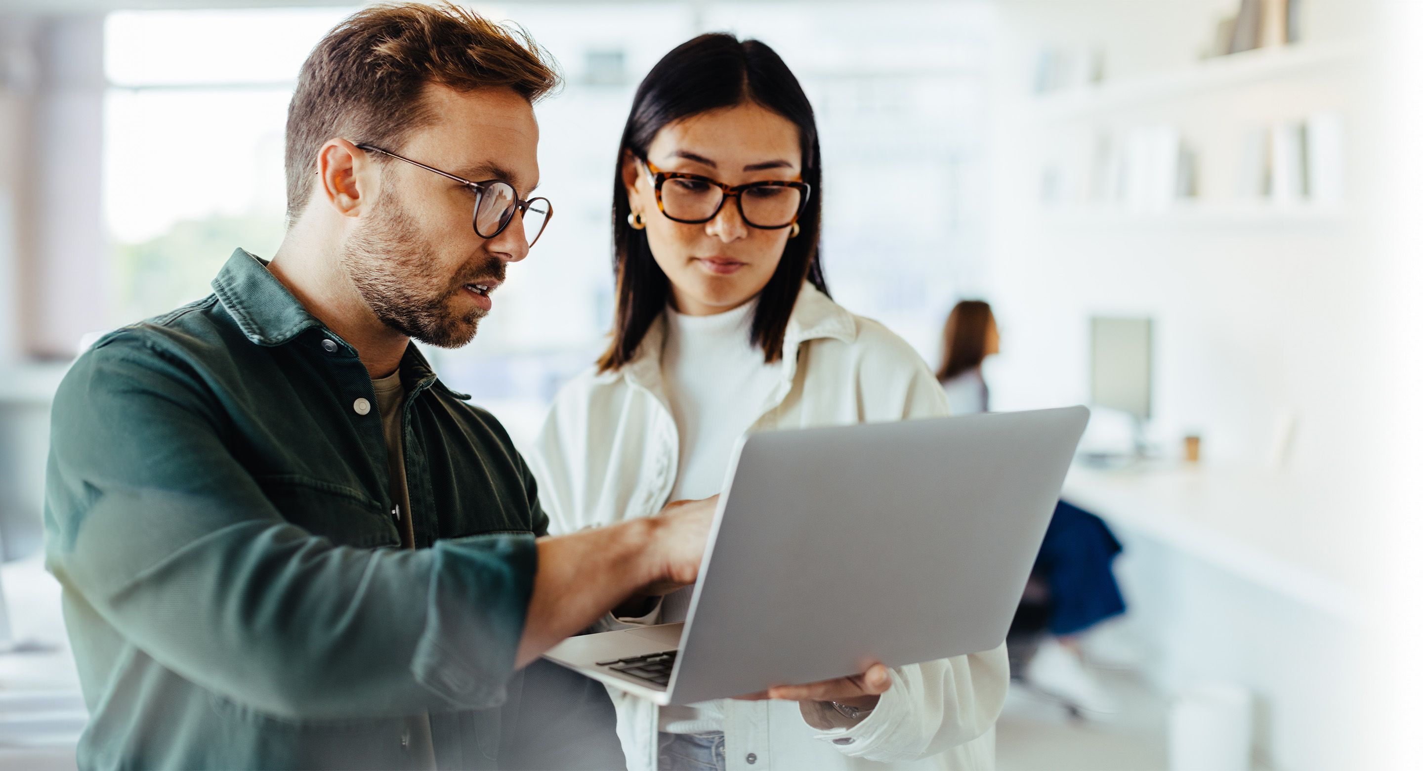 Two colleagues standing together as they look at a laptop screen.
