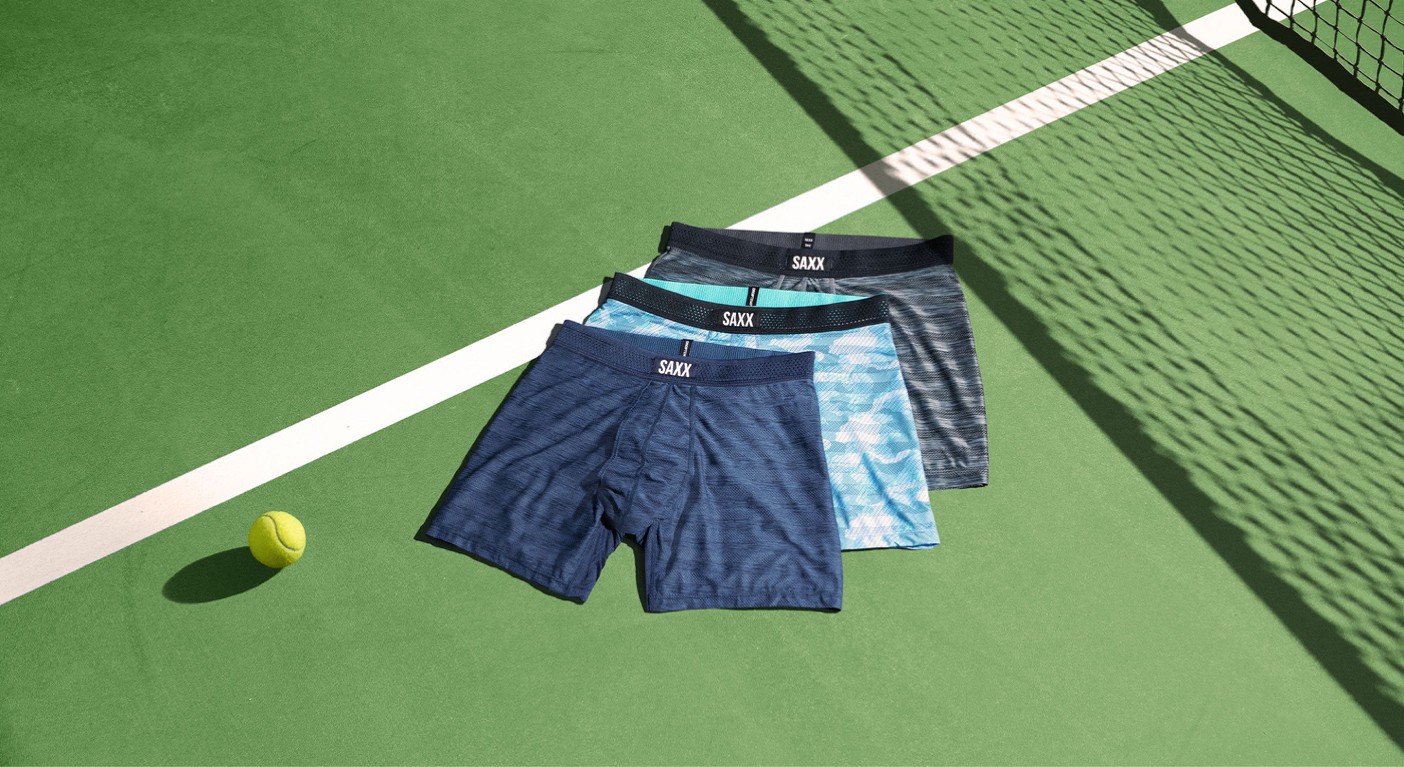 Three pairs of SAXX underwear are laid out on a tennis court.