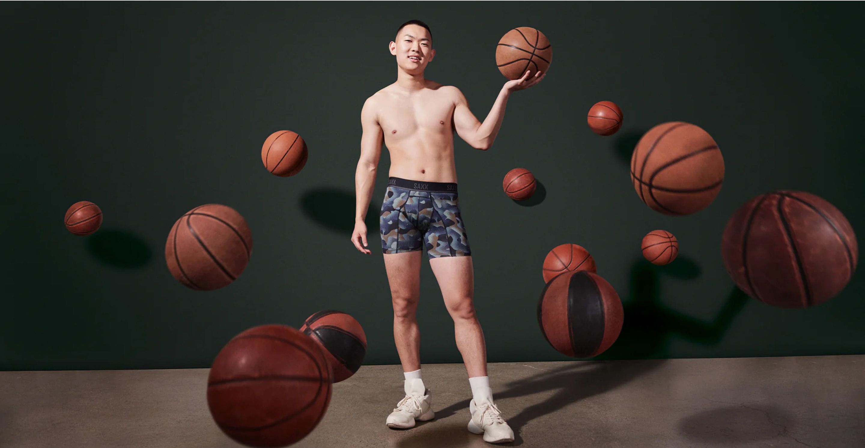 A man wearing SAXX underwear and running shoes holds a basketball.