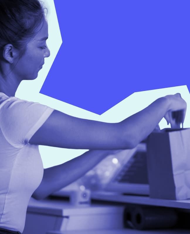 A person working at a retail POS, packing a reusable paper bag.