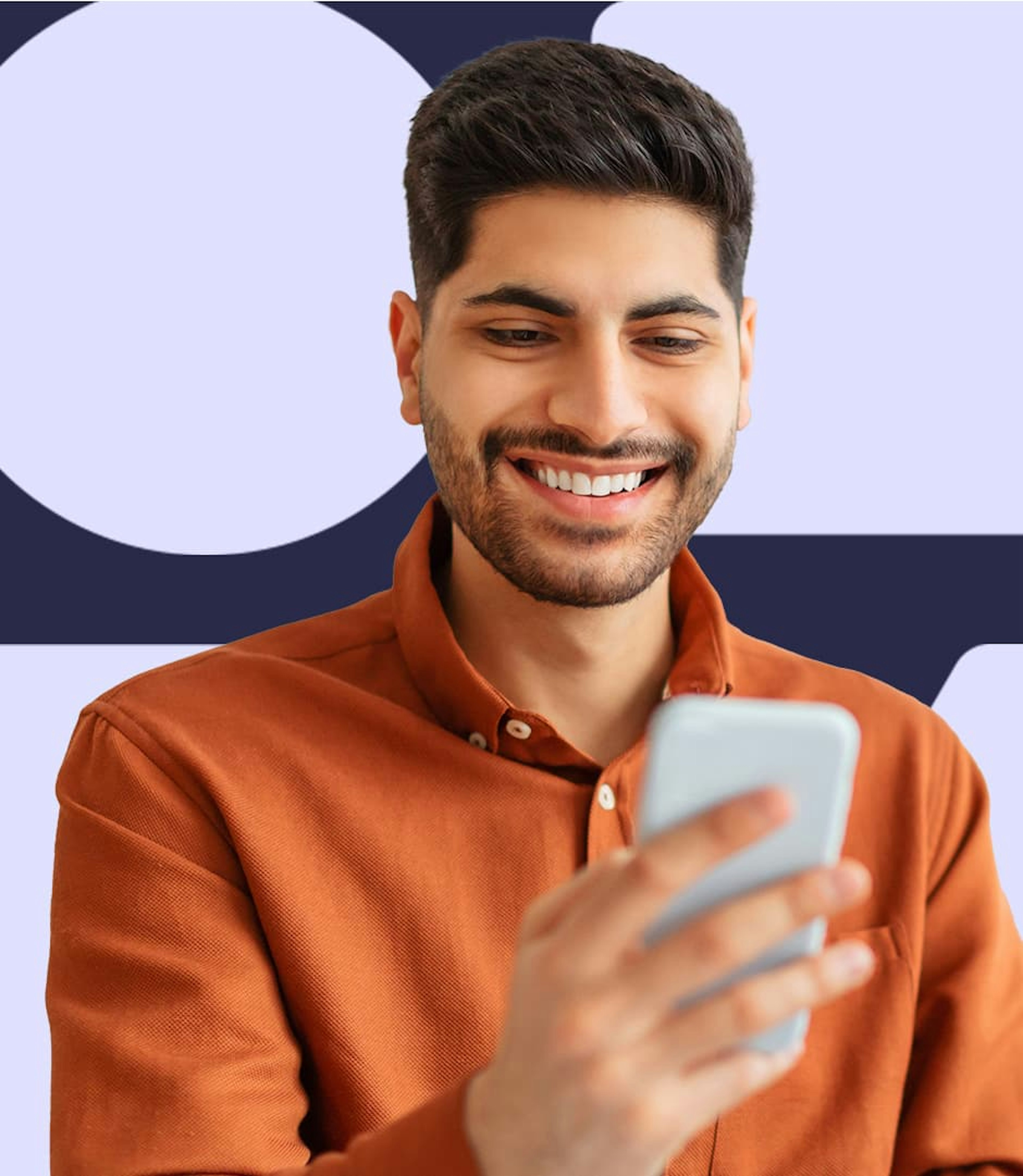 A man in an orange shirt holding a cellphone in one hand and smiling.
