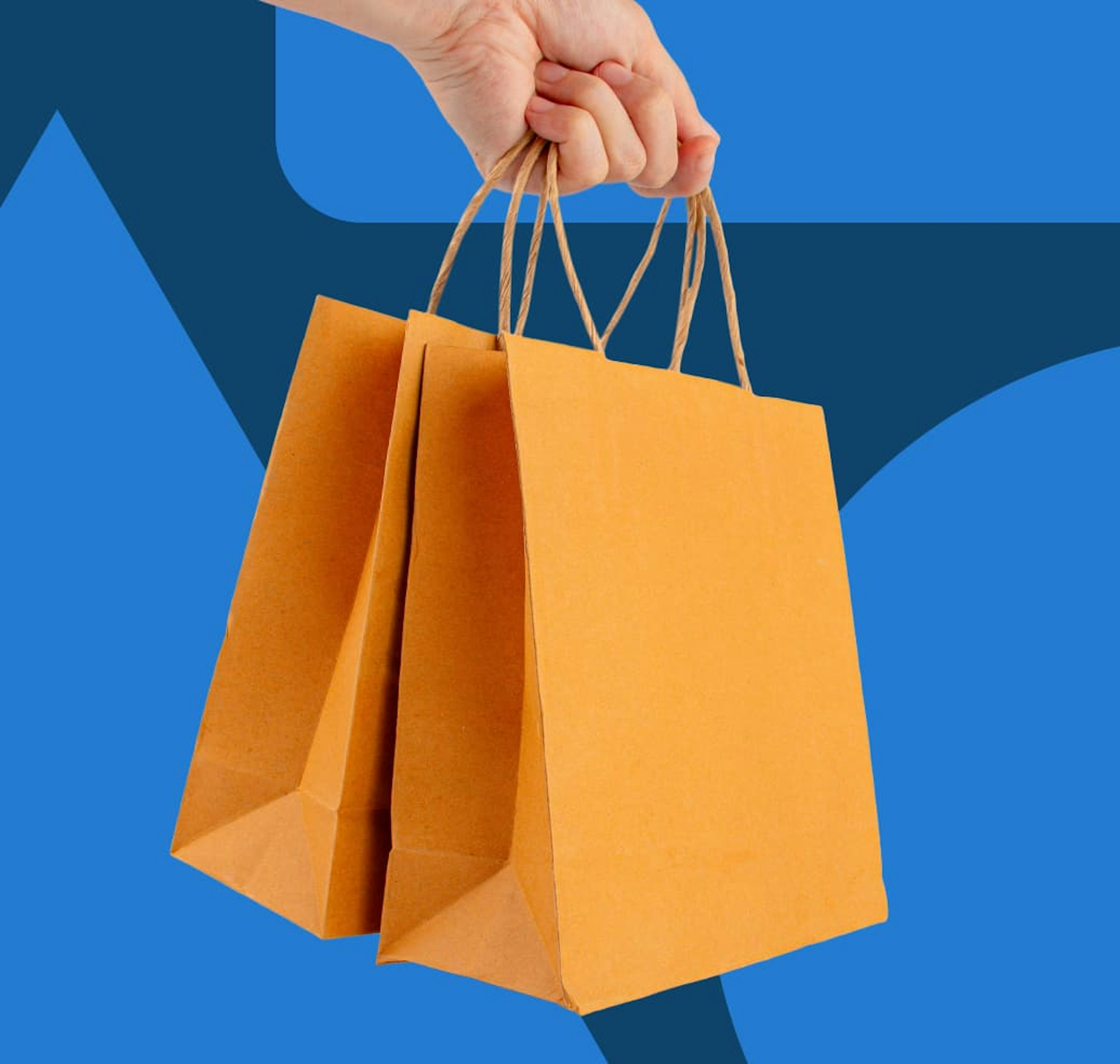 A hand holding two small bright orange shopping bags.
