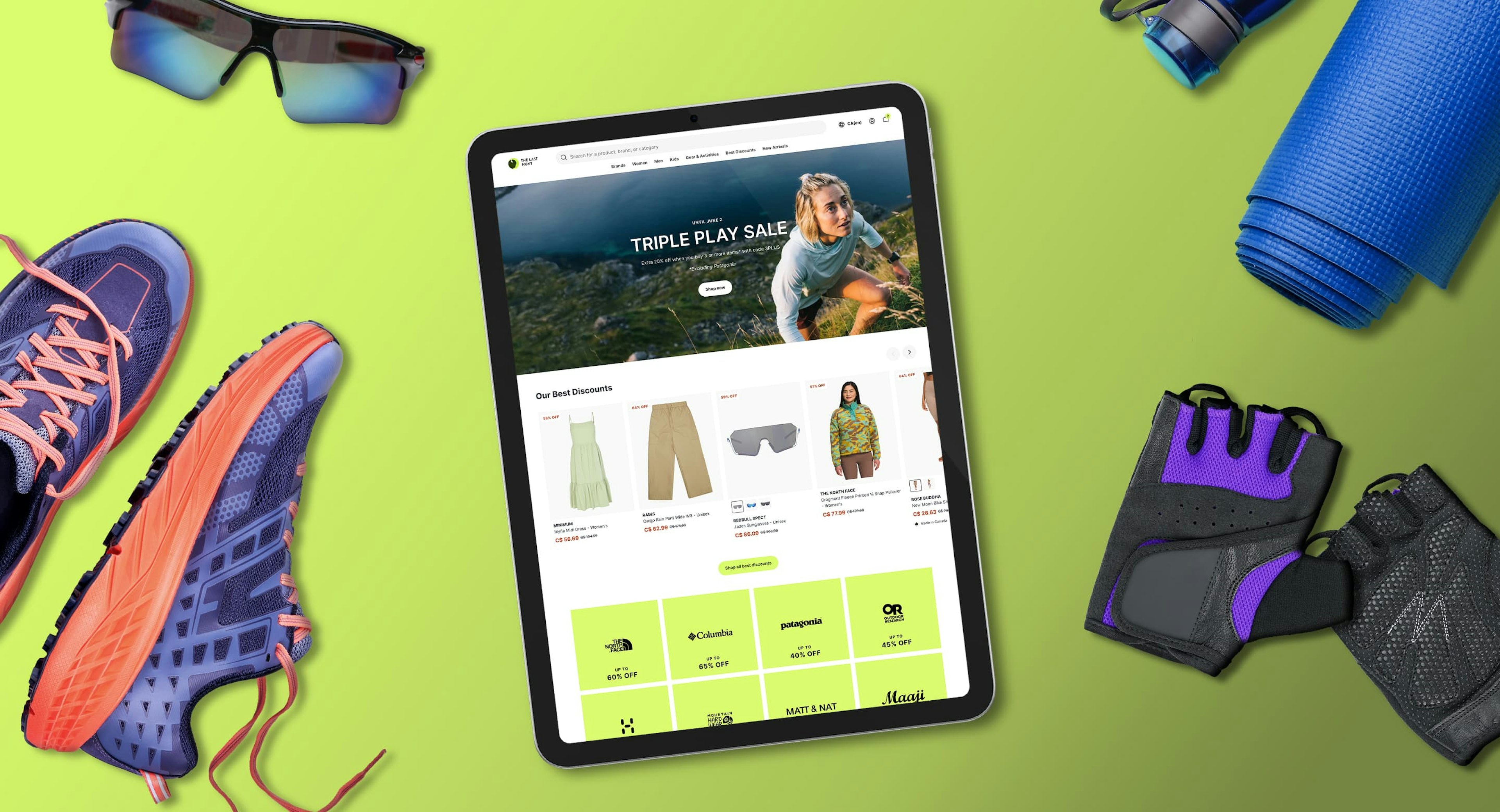 A flatlay of a lime green background with an iPad showing the home page TheLastHunt website, surrounded by running shoes, sports sunglasses, a yoga mat, and hiking gloves.