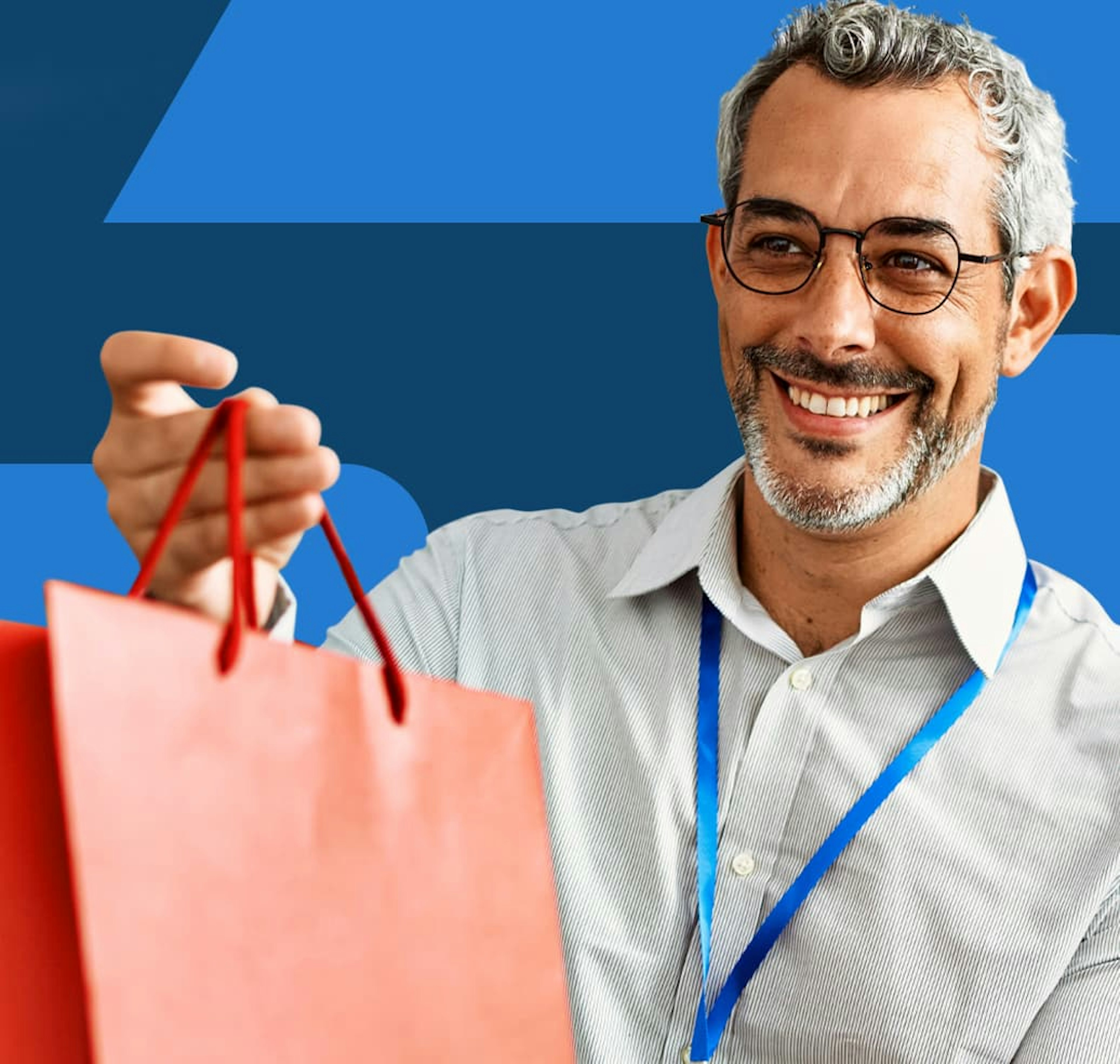 A man wearing a dress shirt is smiling while holding an orange gift bag in one hand.