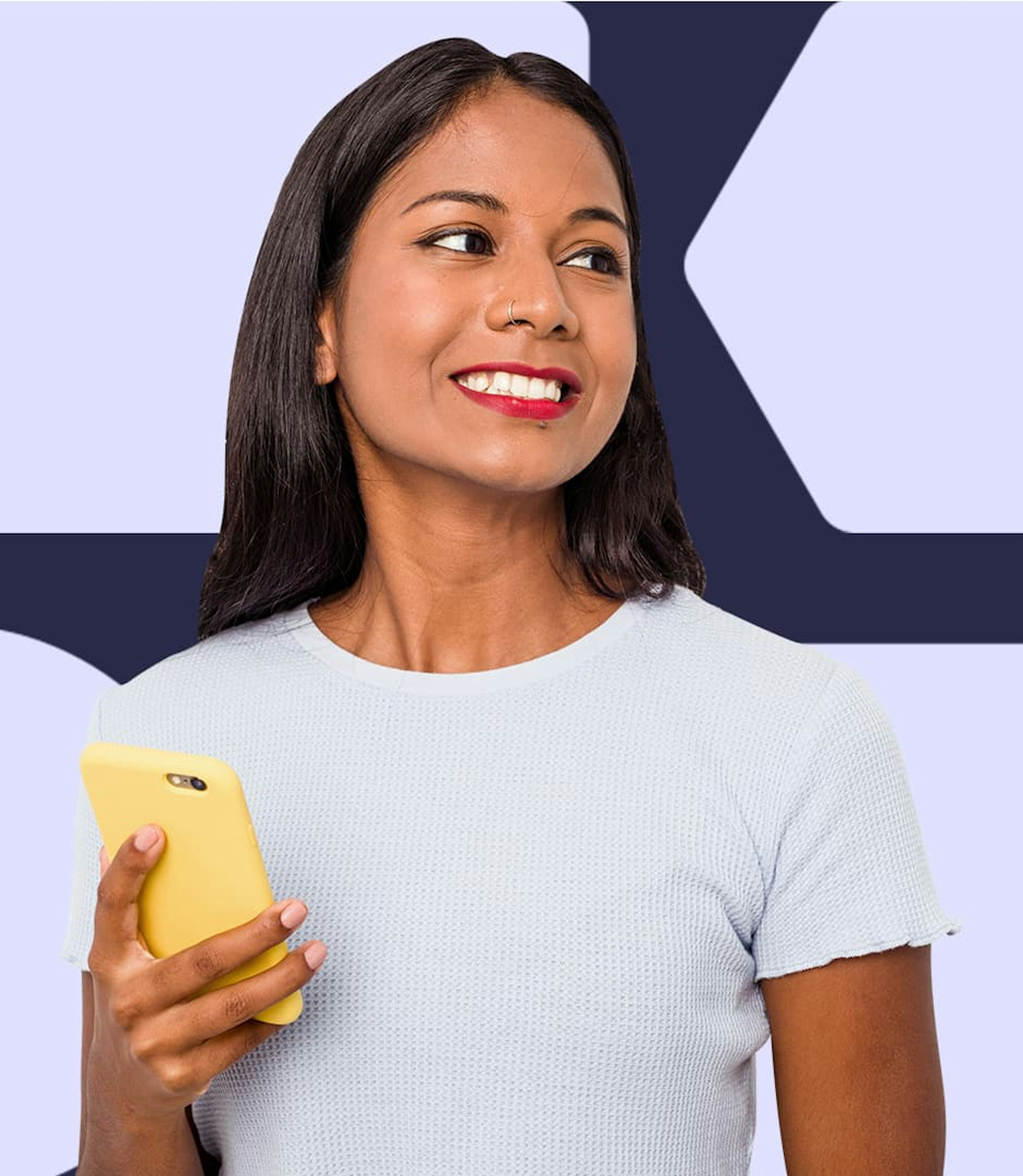 A woman in a white t-shirt is holding a yellow-cased cellphone and smiling off to the side.