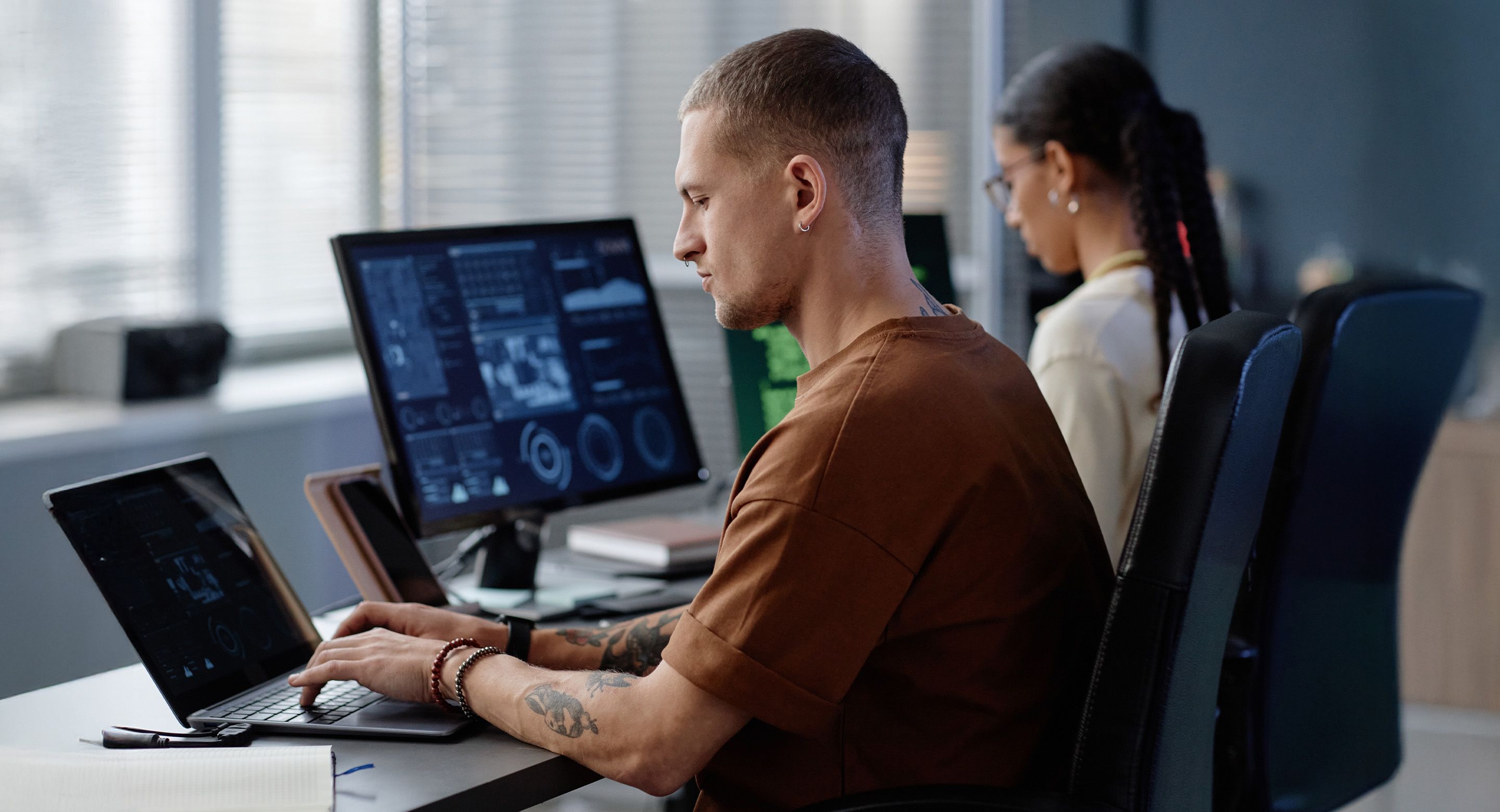 Developers working side by side at desks with analytics dashboards on screens
