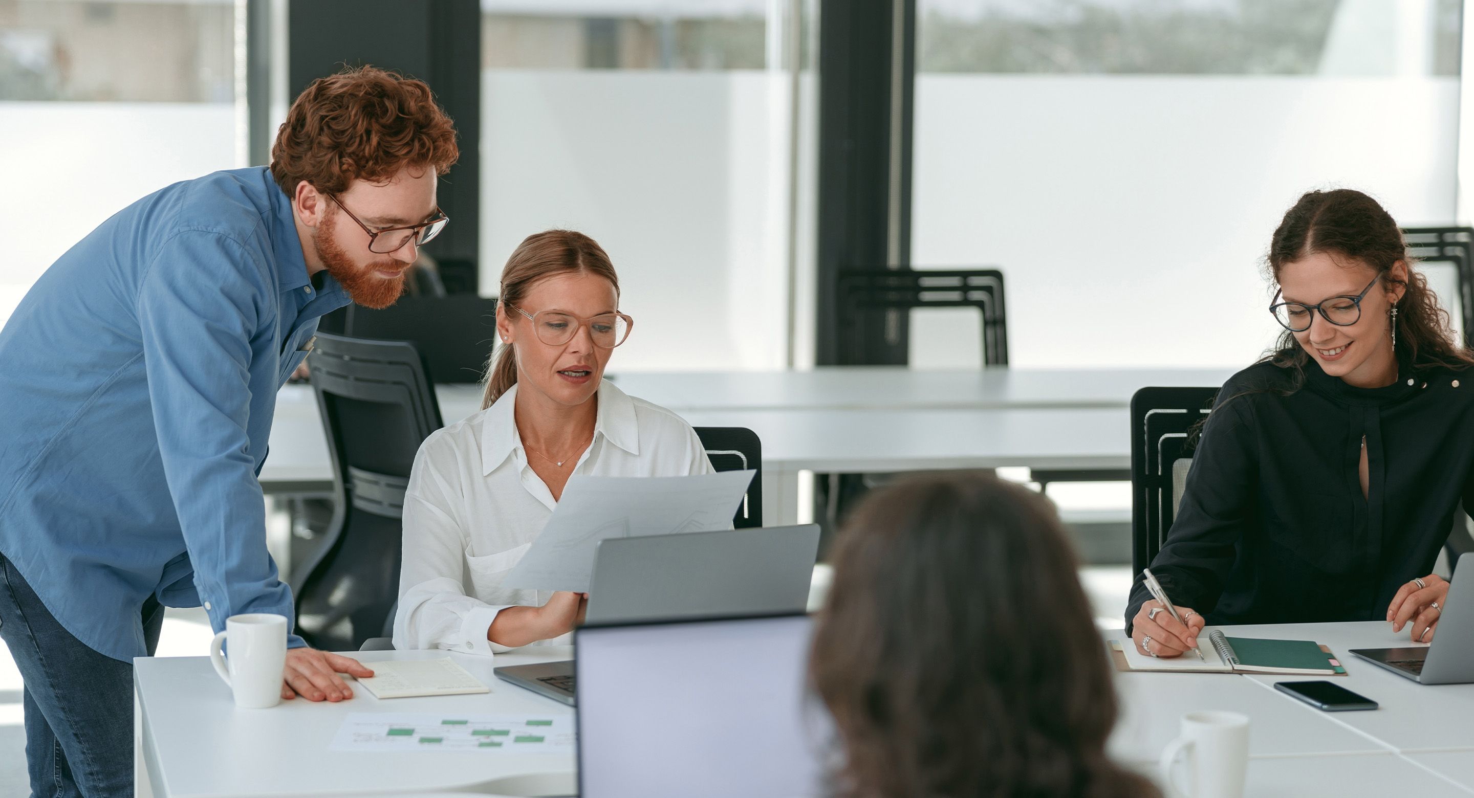 Team collaborating in a modern office, reviewing documents and taking notes during a business meeting.
