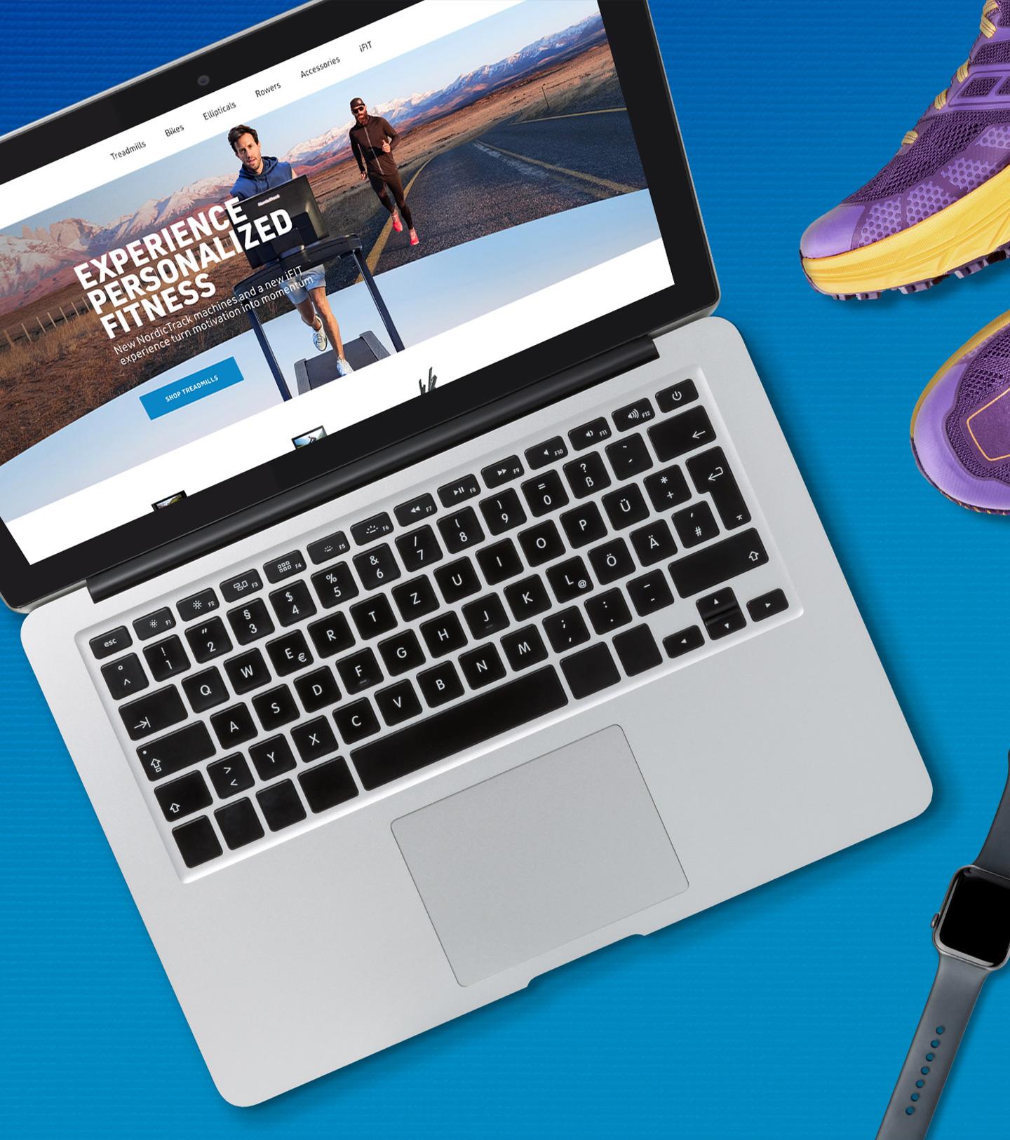 A laptop showing the NordicTrack website on a blue background with running shoes and a smartwatch.