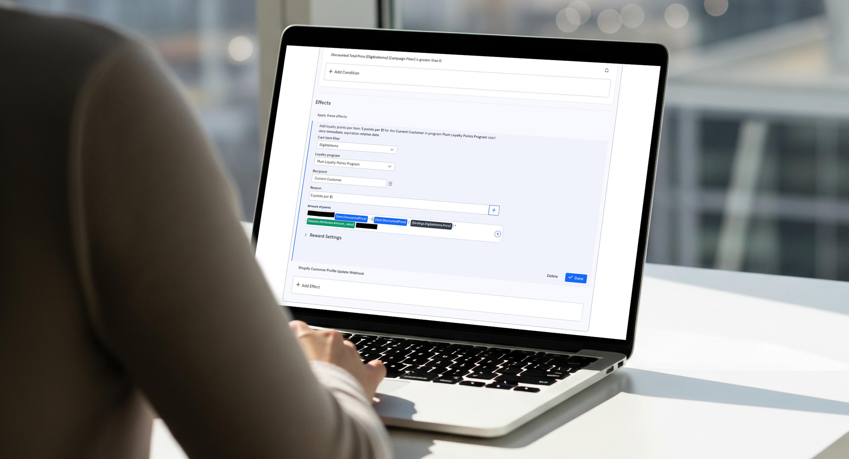 Over-the-shoulder view of a person working on a laptop showing the Talon.One admin interface configuring loyalty point effects for the plum Loyalty Points Program.