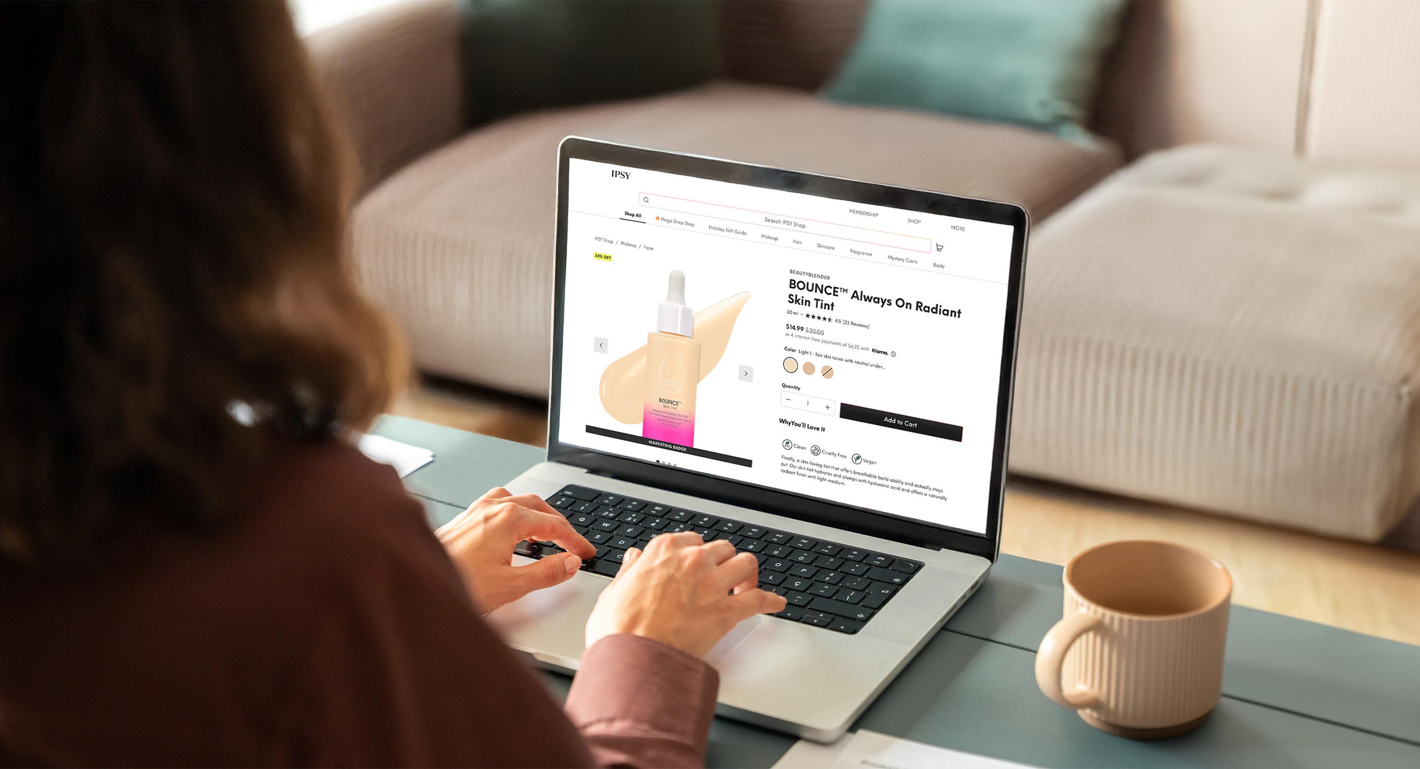 A woman browsing the IPSY website and viewing a beauty product on the laptop with a coffee cup beside it.