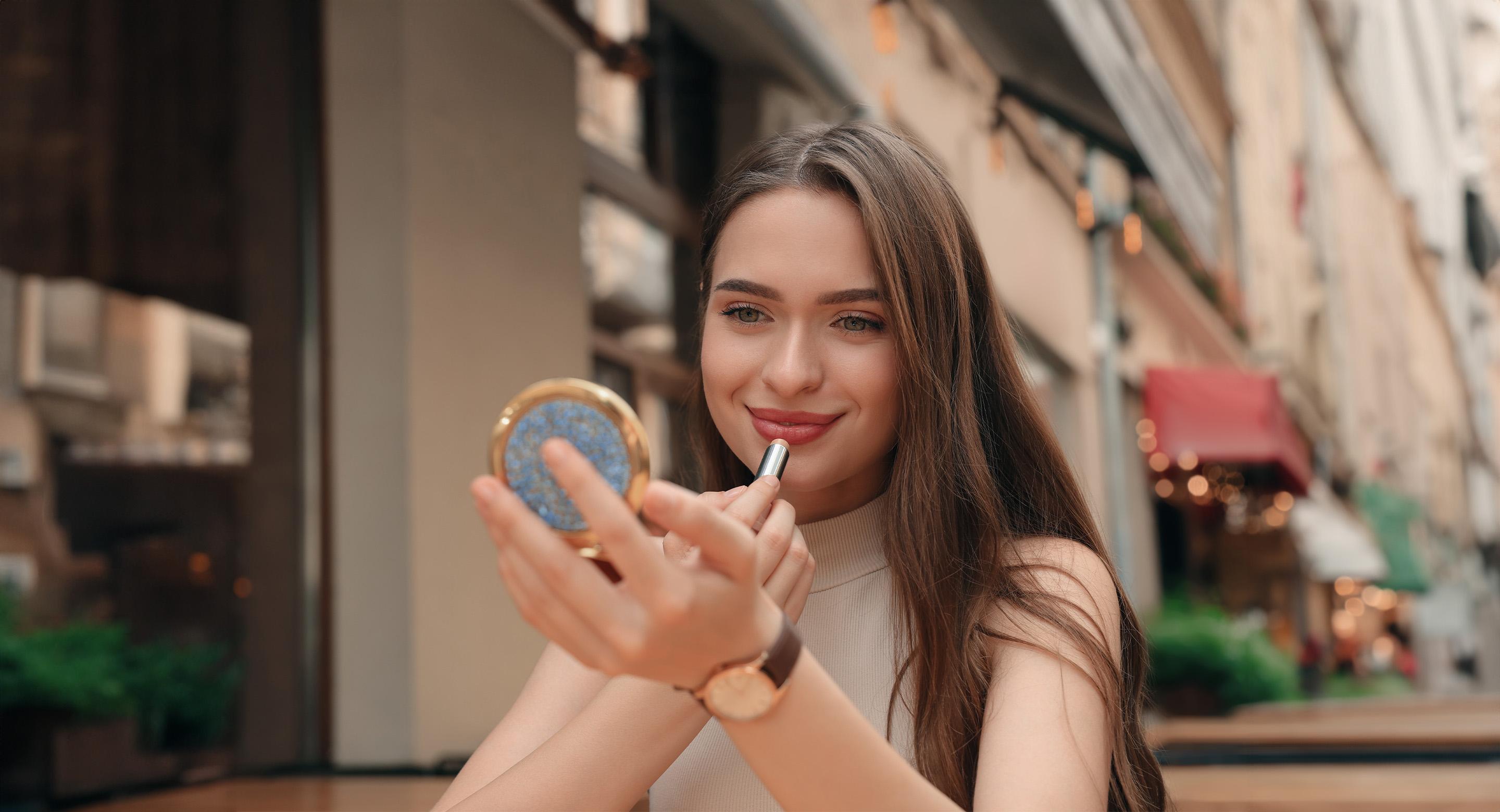 A woman applying lipstick on her lips using a compact mirror.