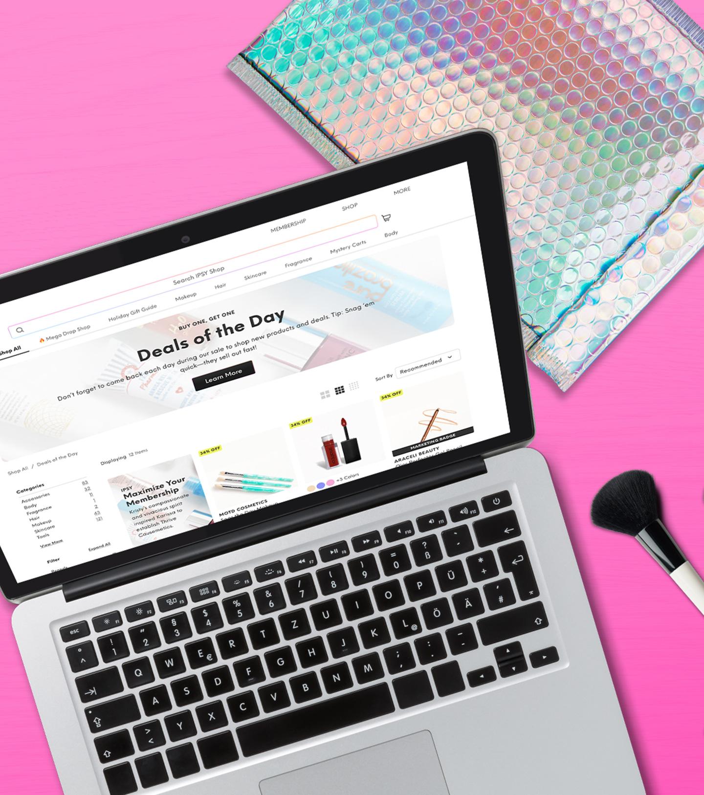 Una laptop mostrando el sitio web de la tienda IPSY sobre un fondo rosa con productos de maquillaje.