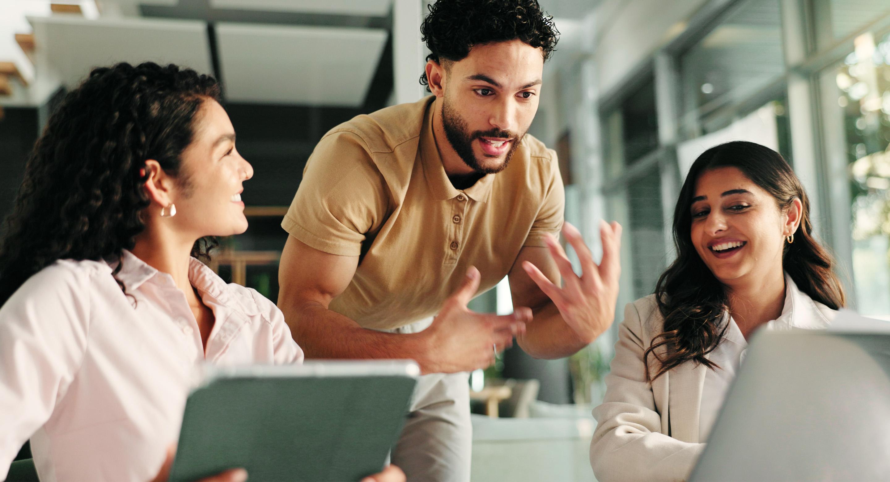 Three coworkers collaborating enthusiastically around a laptop in a modern office.
