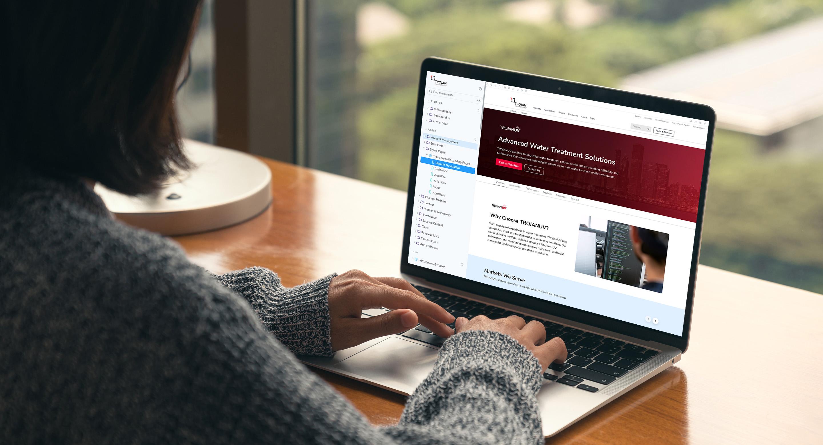 Person typing on a laptop displaying the Trojan Technologies website's TROJANUV product page, with a city skyline visible through the window behind them.