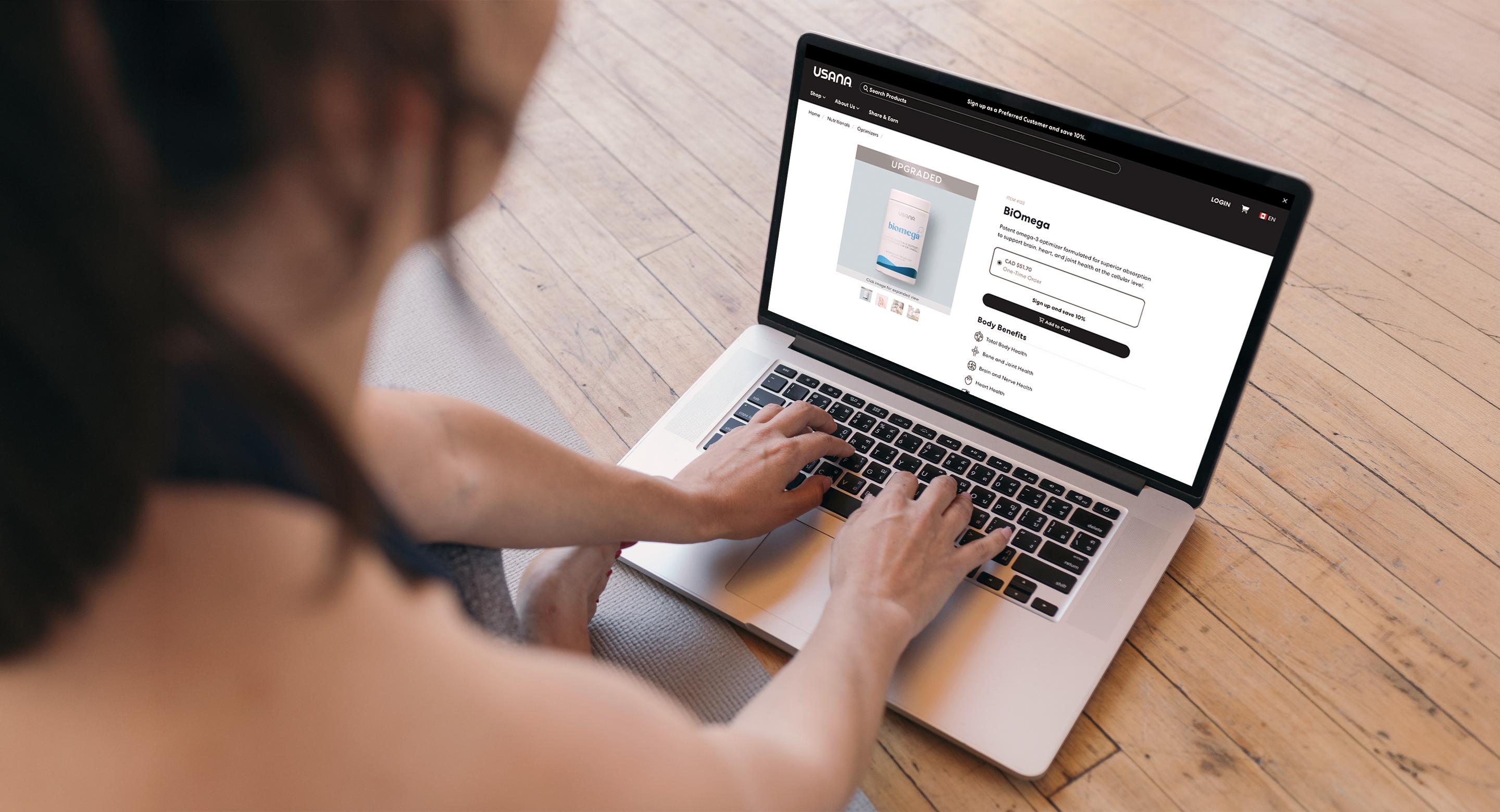 Over-the-shoulder view of a person on a laptop viewing a USANA BiOmega product page.