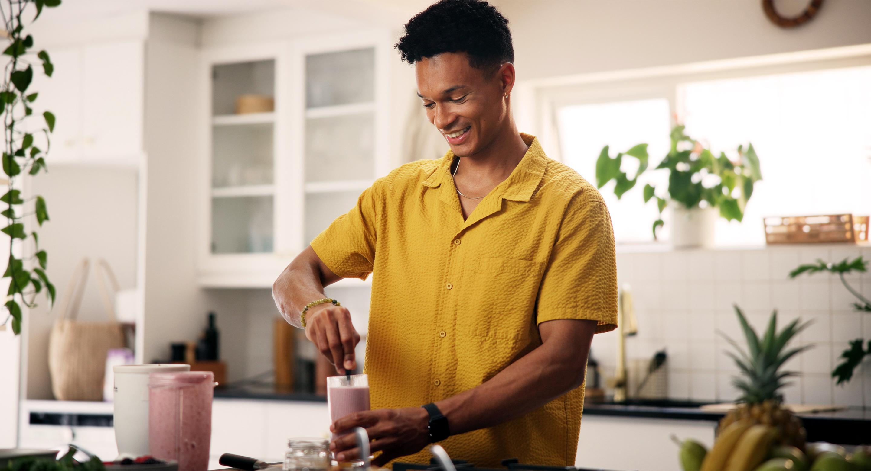 A smiling man preparing a USANA nutrition shake in a bright kitchen.