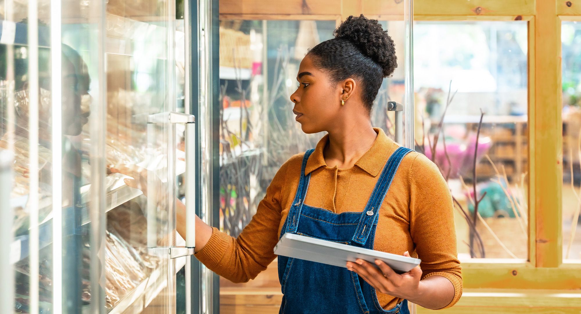 Store employee uses a tablet while selecting products from a refrigerated food display.