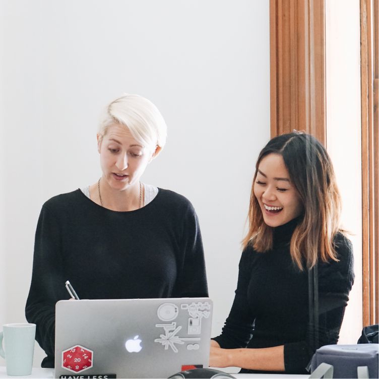 Two people working together at a desk, looking at a laptop and taking notes.