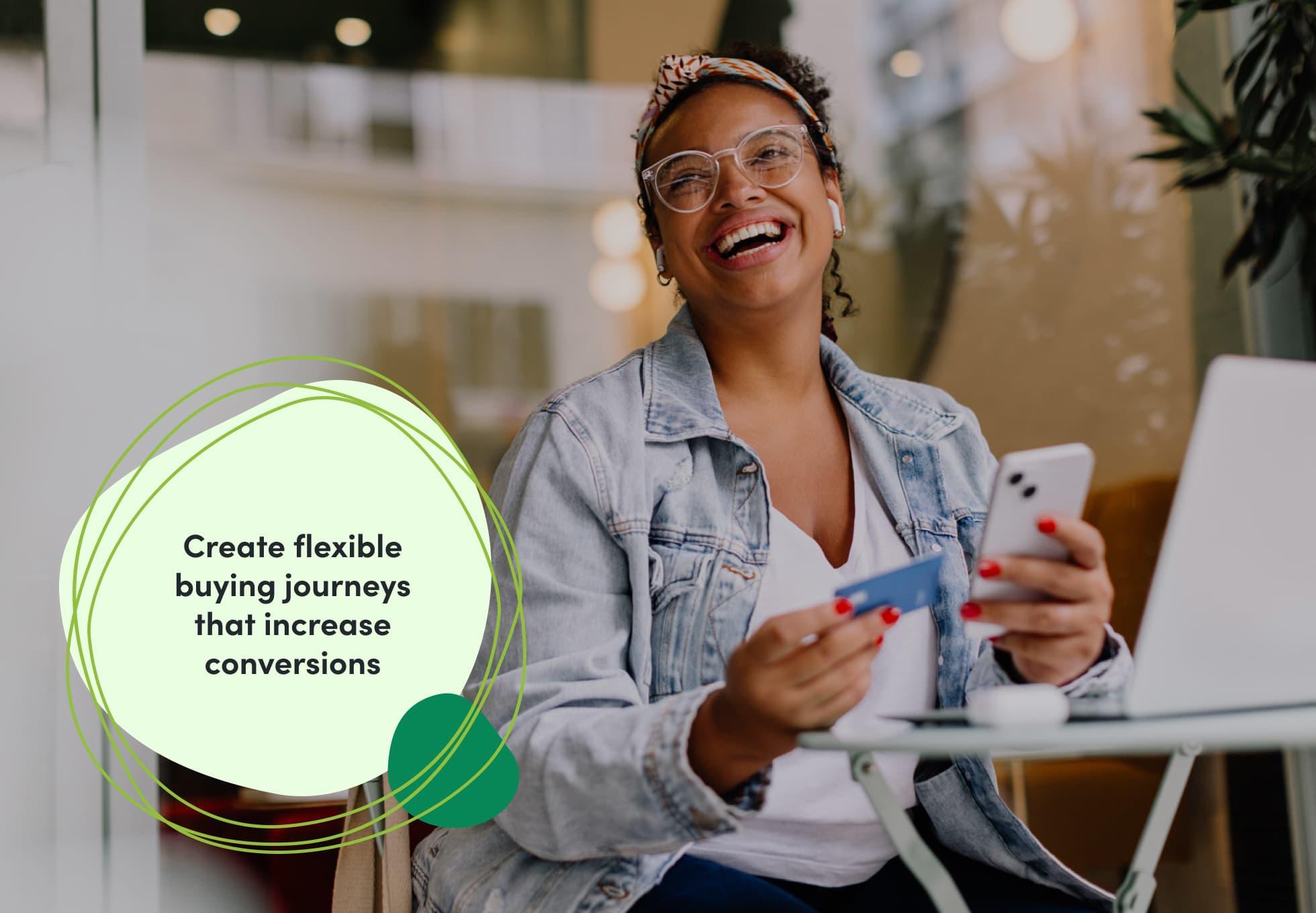 A person sitting with their laptop and smiling, holding their cellphone in one hand and a credit card in another. The imposed text reads "Create flexible buying journeys that increase conversions."