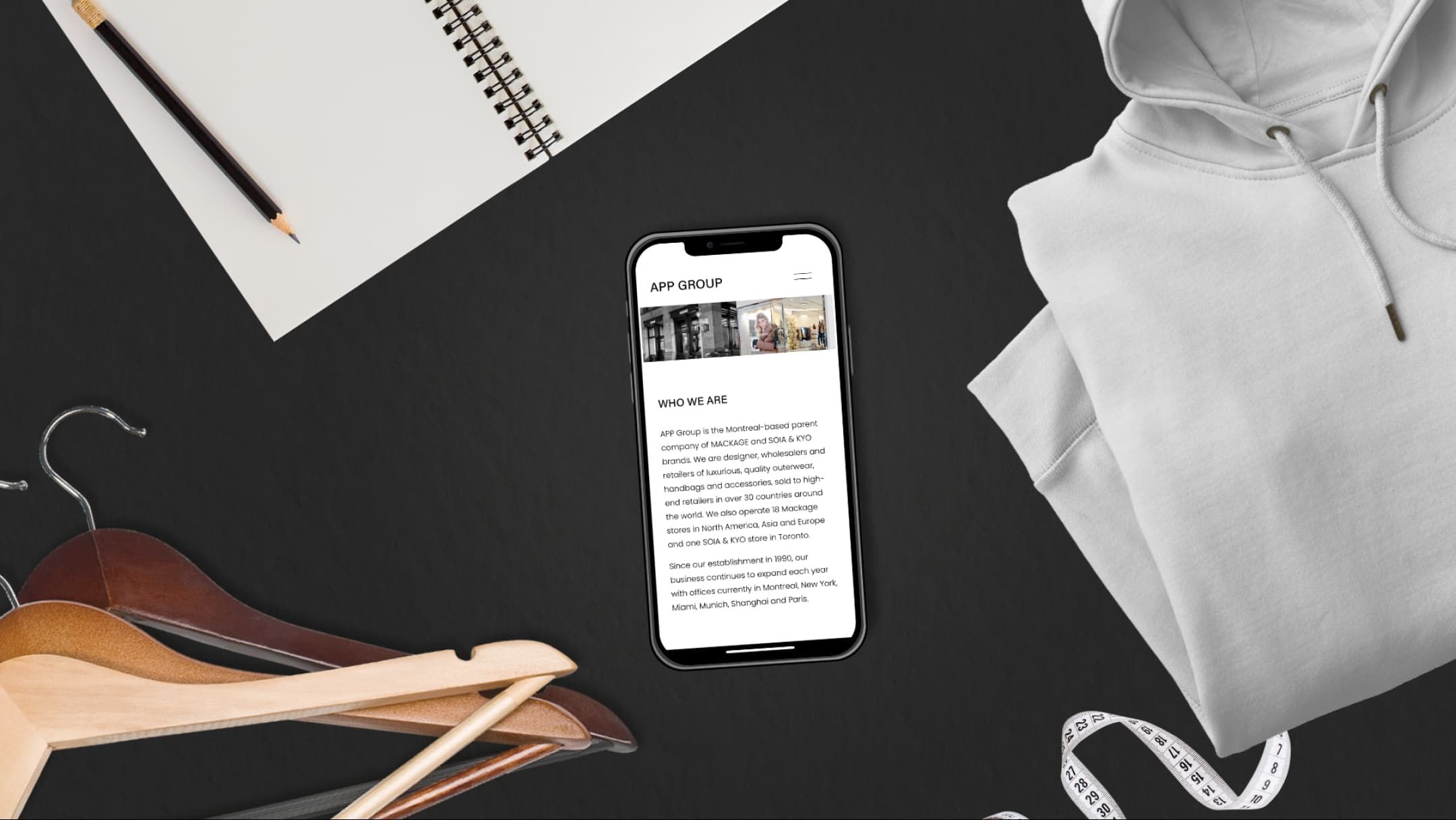 Flatlay with an iPhone with the APP Group's website on screen, surrounded by clothing, hangers, and a tape measure.