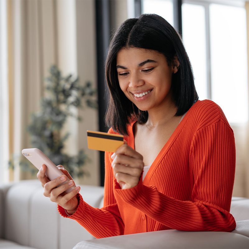 A woman holds a credit card in one hand and a smartphone in the other.