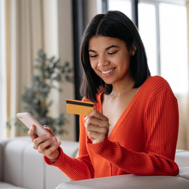 A woman holds a credit card in one hand and a smartphone in the other.