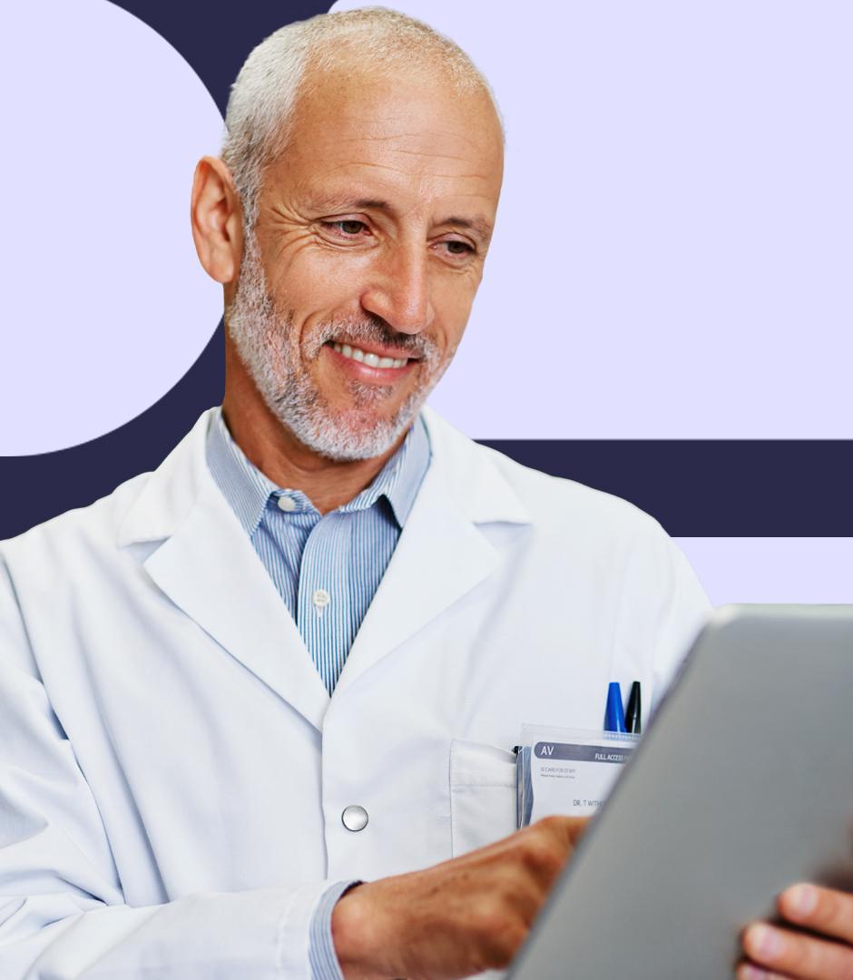 An older male doctor in a white coat, holding a tablet and smiling as he reviews information.