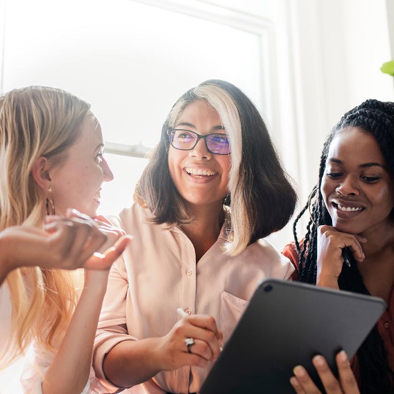 Photo of three women discussing something while one holds a tablet and stylus
