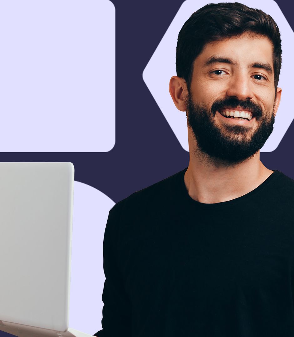 A man with a beard looks straight into the camera and smiles with a laptop in his hands.