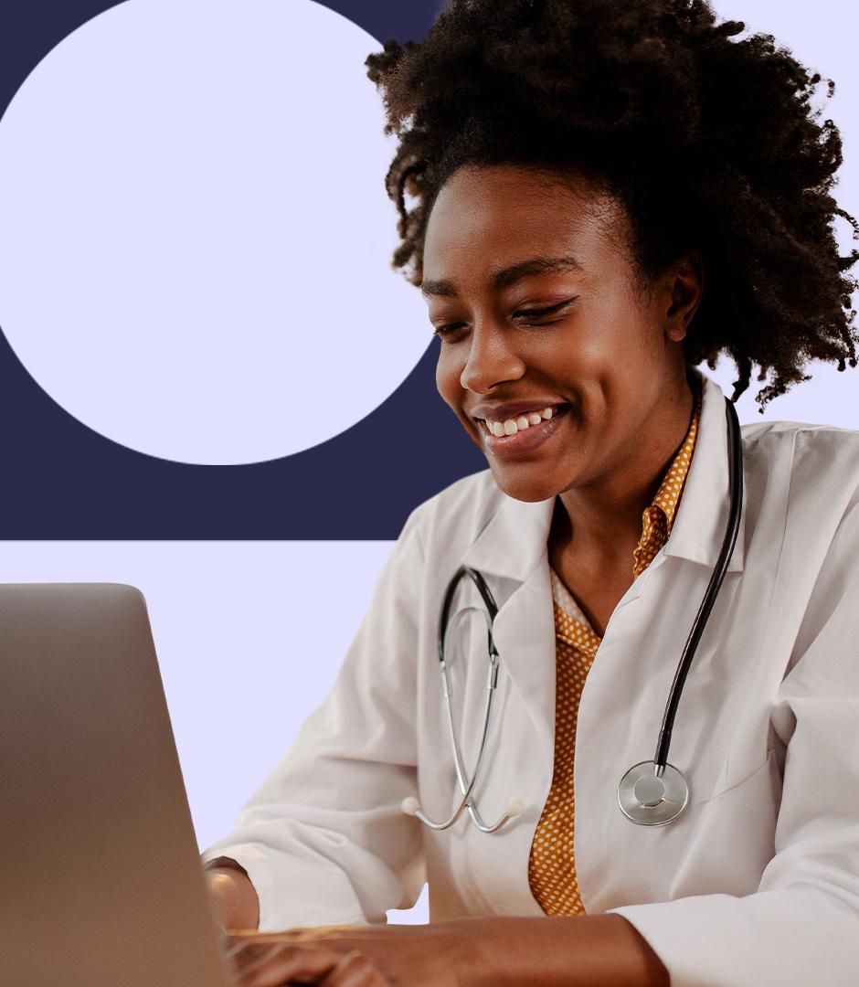 A smiling female doctor with a stethoscope around her neck types on a laptop, appearing engaged and focused.