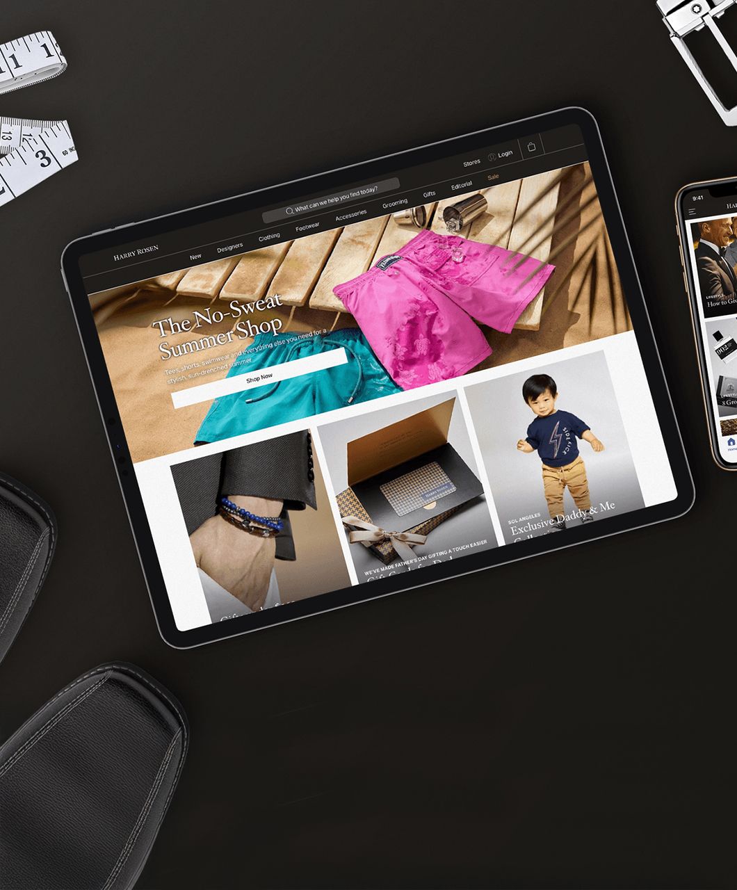 Tablet displaying an online fashion store featuring summer clothing and accessories, placed on a black desk with measuring tape and other items nearby.