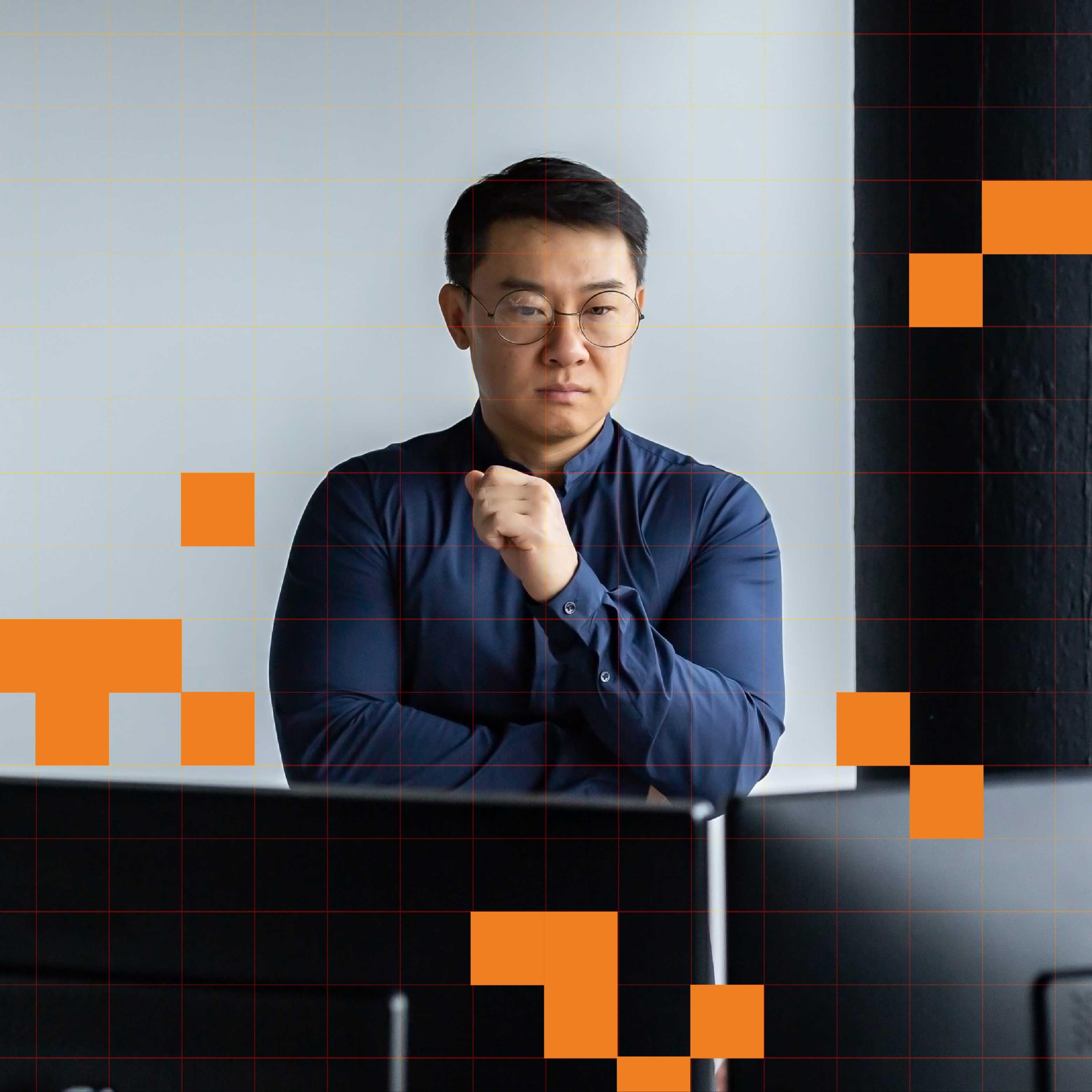 A person stands in front of two computer screens, assessing.