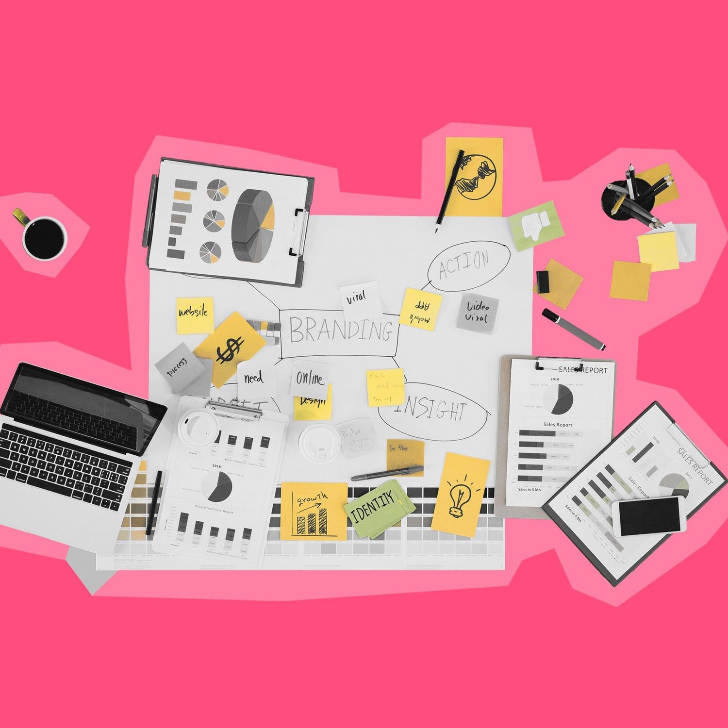 A tabletop filled with branding strategy materials, sticky notes, and digital devices, set against a pink background.