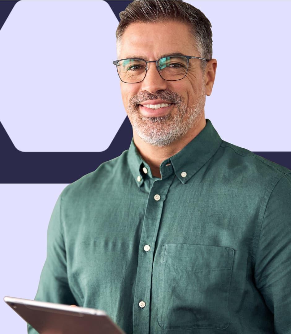 A man in a green button down shirt is holding an iPad in his hands and smiling while looking up.