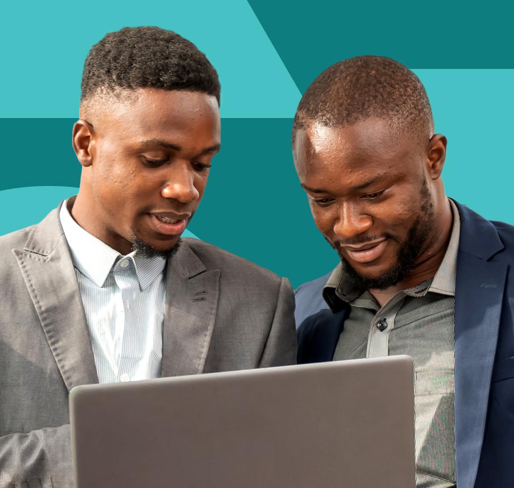 Two men in suits smile and engage as they collaborate over a laptop.