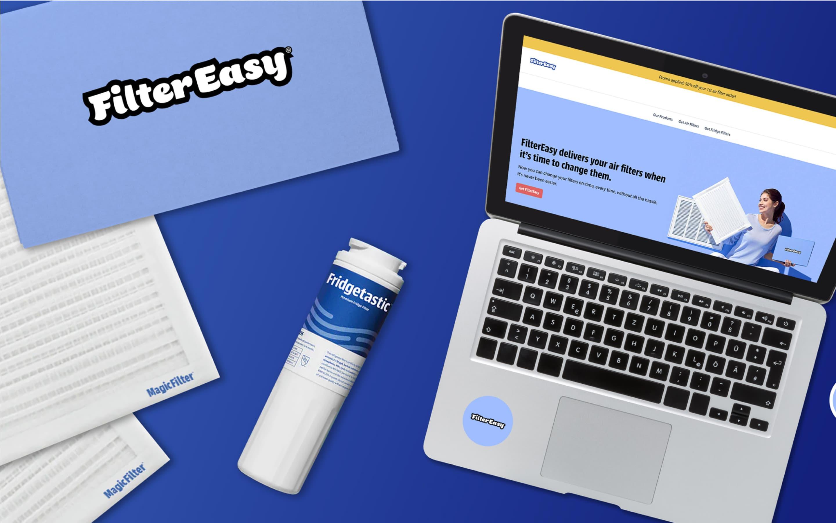 Flatylay featuring a FilterEasy subscription box, a Fridgetastic filter, two Magic Filters, and a laptop screen with the FilterEasy homepage on display.